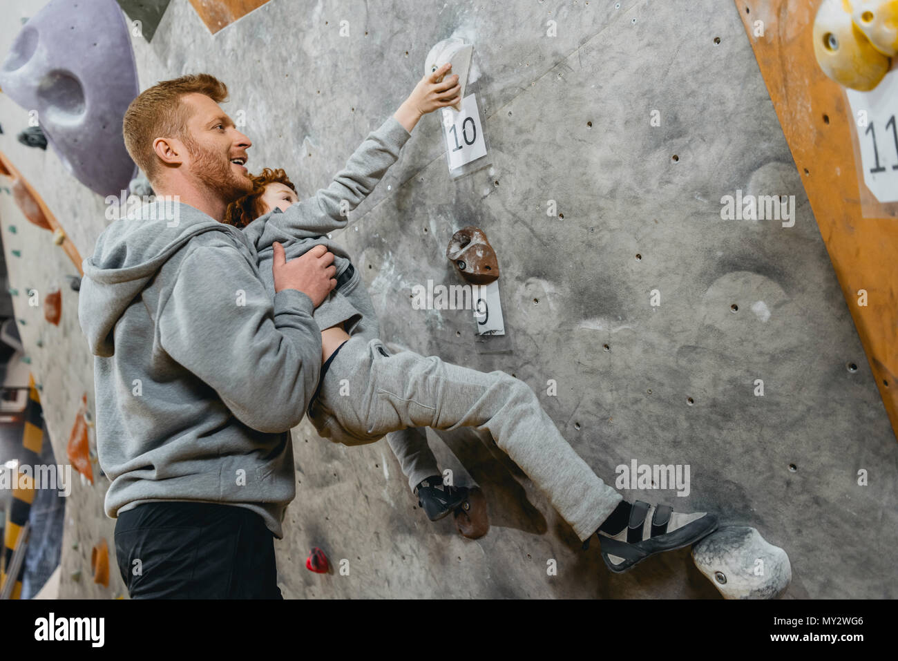 Jeune papa d'enseigner son petit fils comment escalader un mur avec grips at gym Banque D'Images