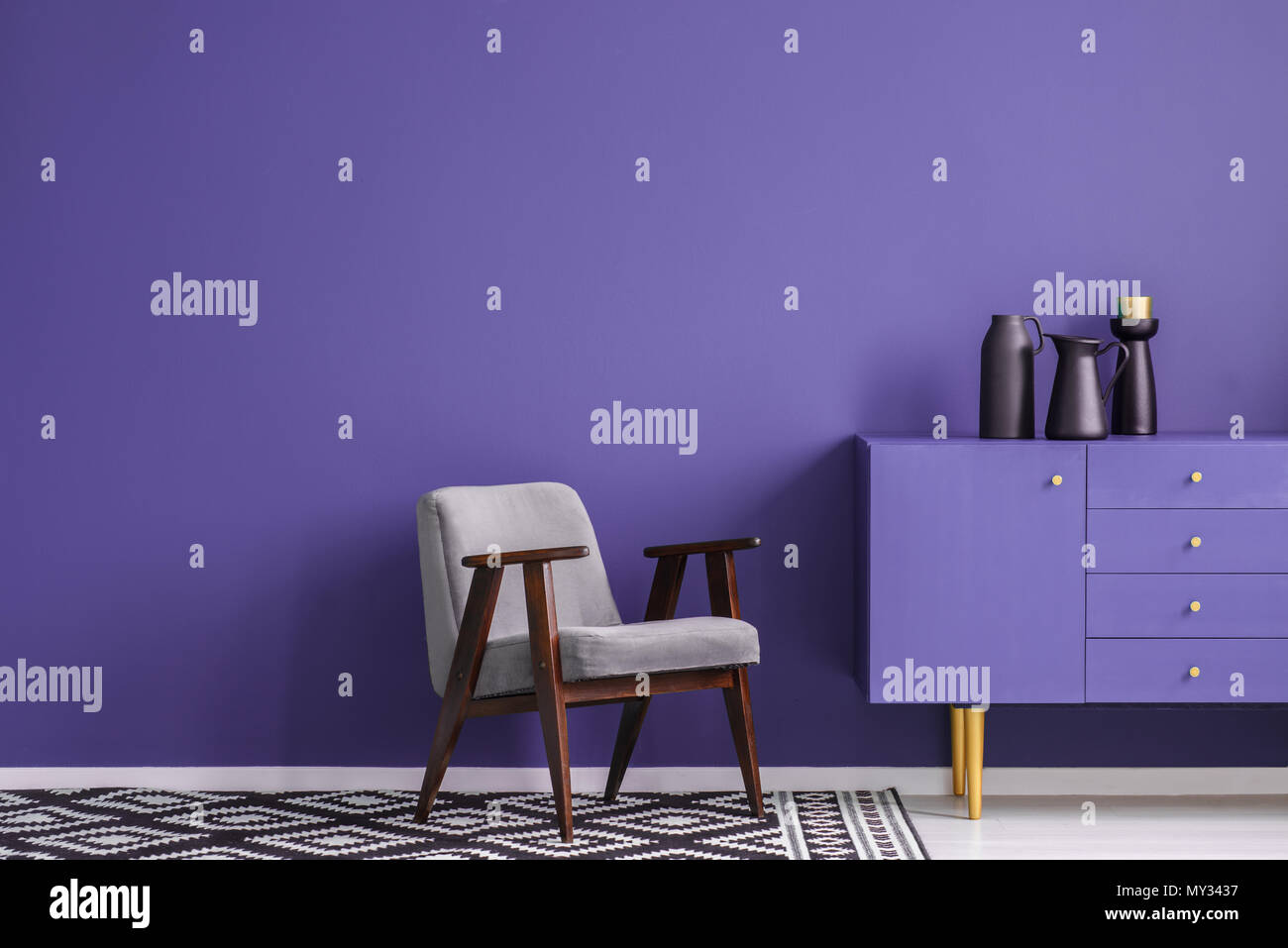 Fauteuil gris sur moquette à motifs à côté du cabinet noir violet avec vase dans le salon intérieur avec copie espace Banque D'Images