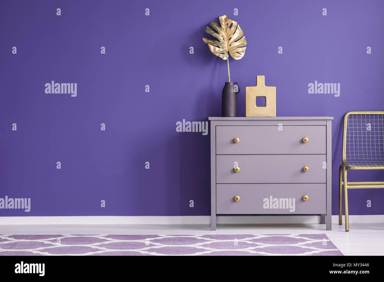 Vase d'or sur violet cabinet à côté d'une chaise dans la salle de séjour intérieur avec des tapis à motifs Banque D'Images