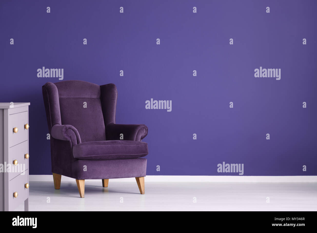 Fauteuil en velours pourpre violet contre mur dans un salon intérieur avec cabinet et copy space Banque D'Images