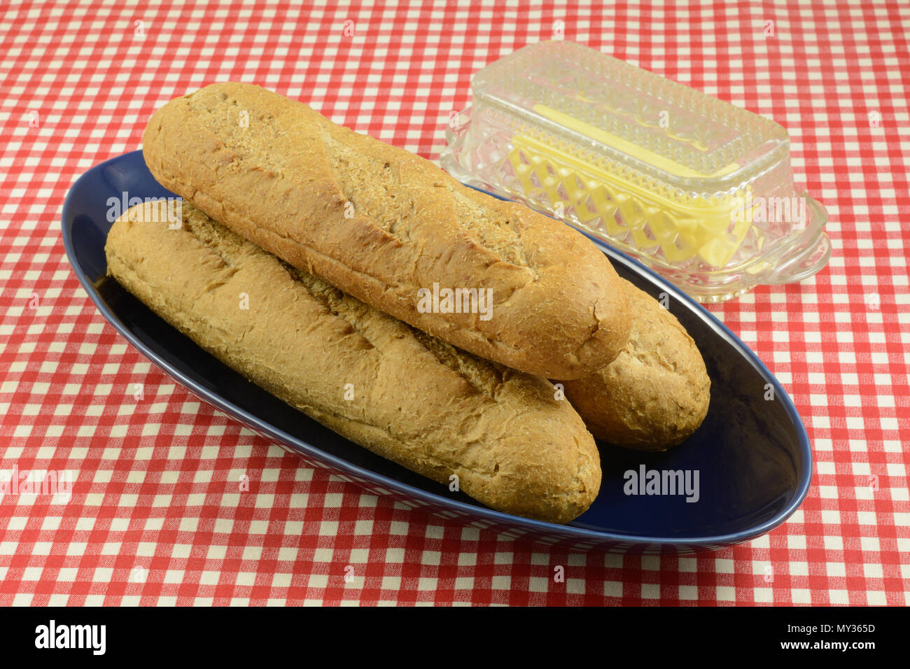 Miches de pain de blé entier pour sandwichs sous-marin sur plateau bleu avec du beurre dans du verre beurrier Banque D'Images