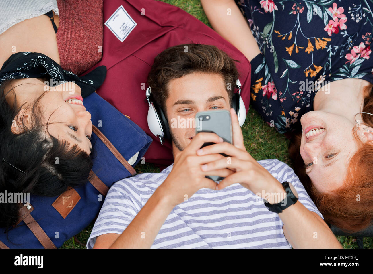 Jeune homme allongé sur l'herbe avec des amis, à l'aide de smartphone et listening to headphones Banque D'Images