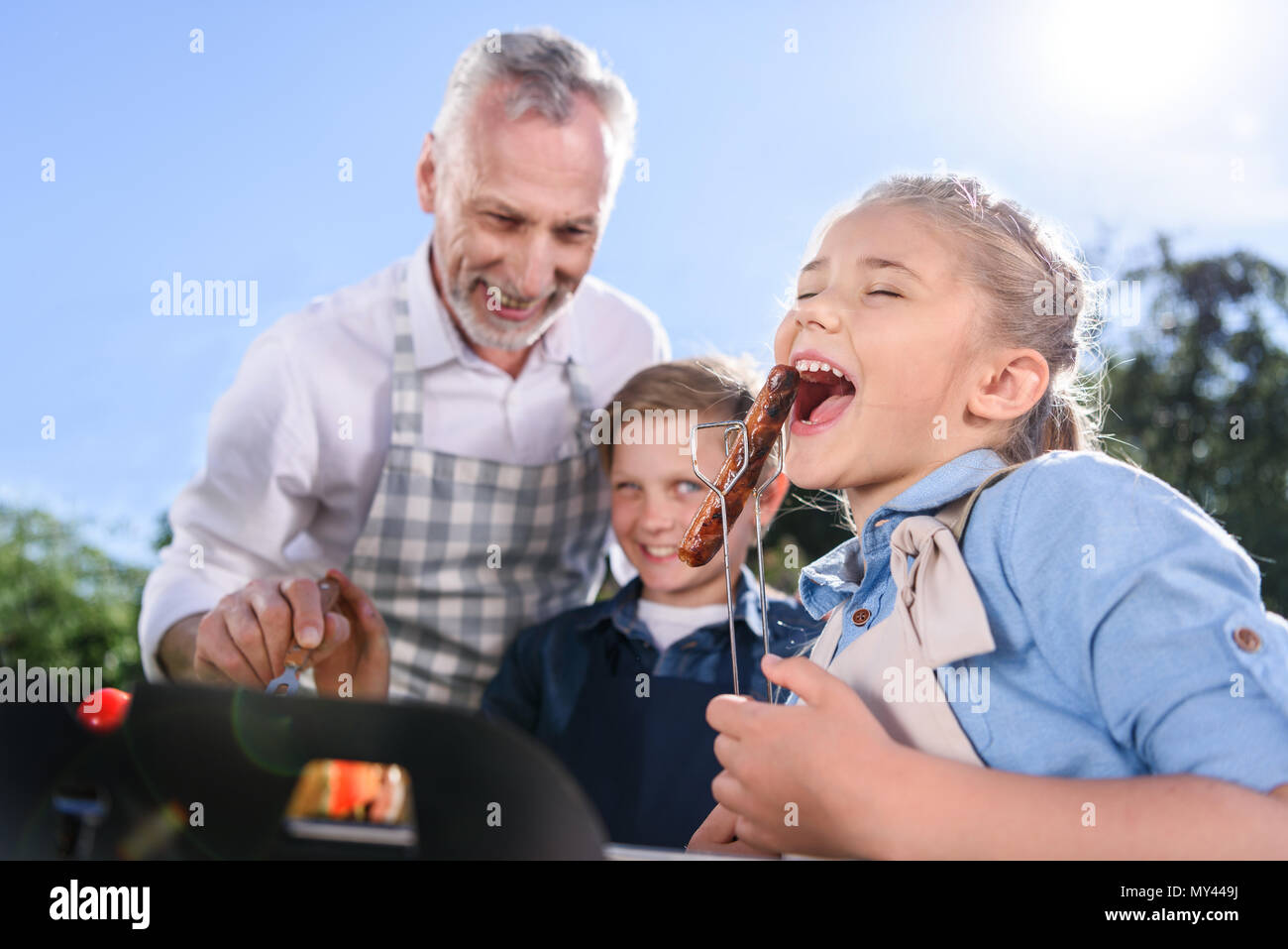 Petits-enfants avec grand-père manger de saucisses grillées sur l'extérieur, pique-nique Banque D'Images