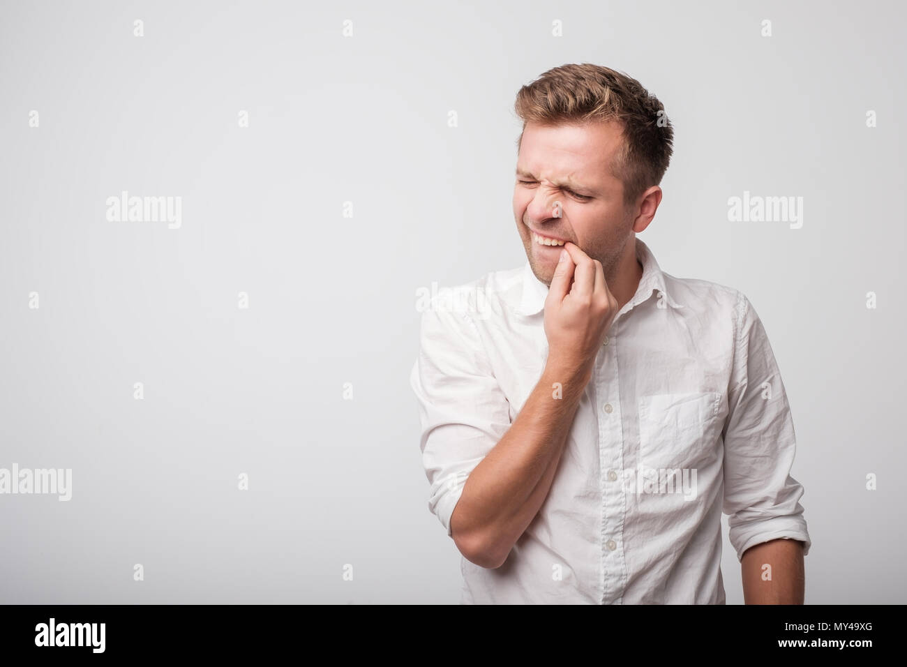 Young caucasian gars en chemise blanche à essayer de nettoyer les dents avec acharnement. Banque D'Images