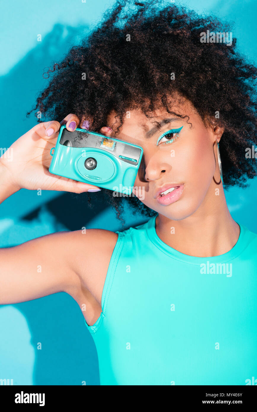 Beau modèle afro posant en maillot bleu avec vintage photo, caméra sur turquoise Banque D'Images