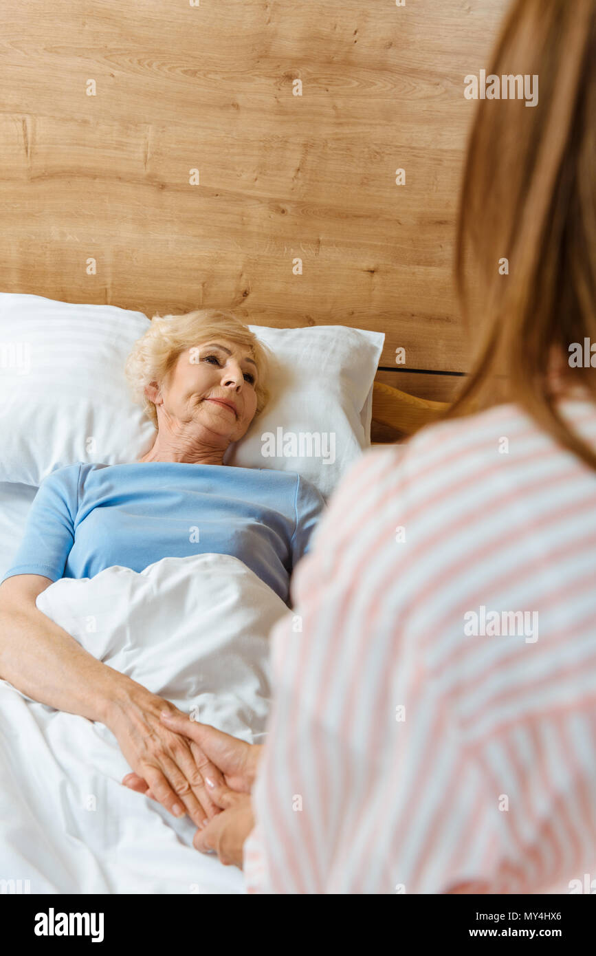 Woman dans un lit d'hôpital et la tenue de main d'un jeune fille assise sur son lit Banque D'Images