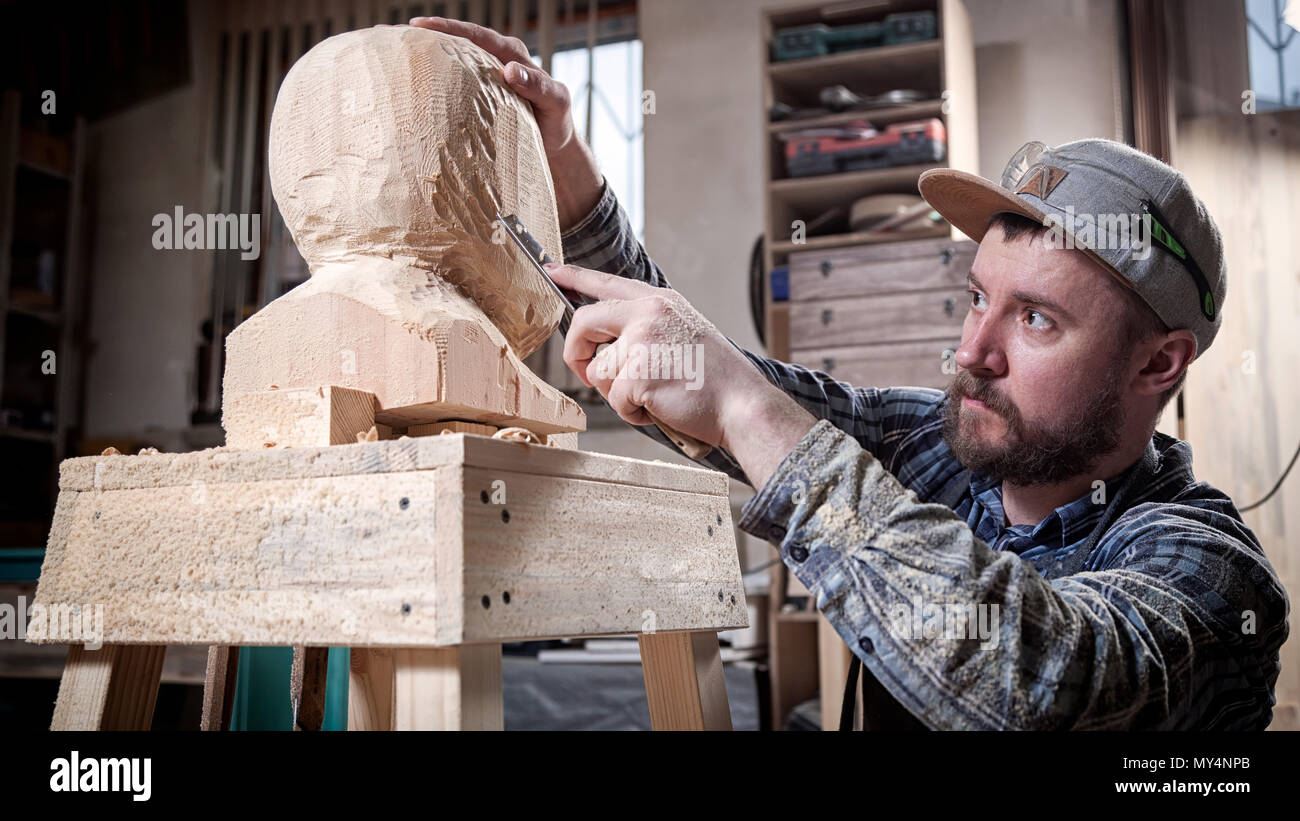 Jeune homme dans un menuisier scies vêtements de travail à la tête d'un homme avec un arbre , à l'aide d'un burin dans l'atelier, autour d'un lot d'outils pour le travail Banque D'Images