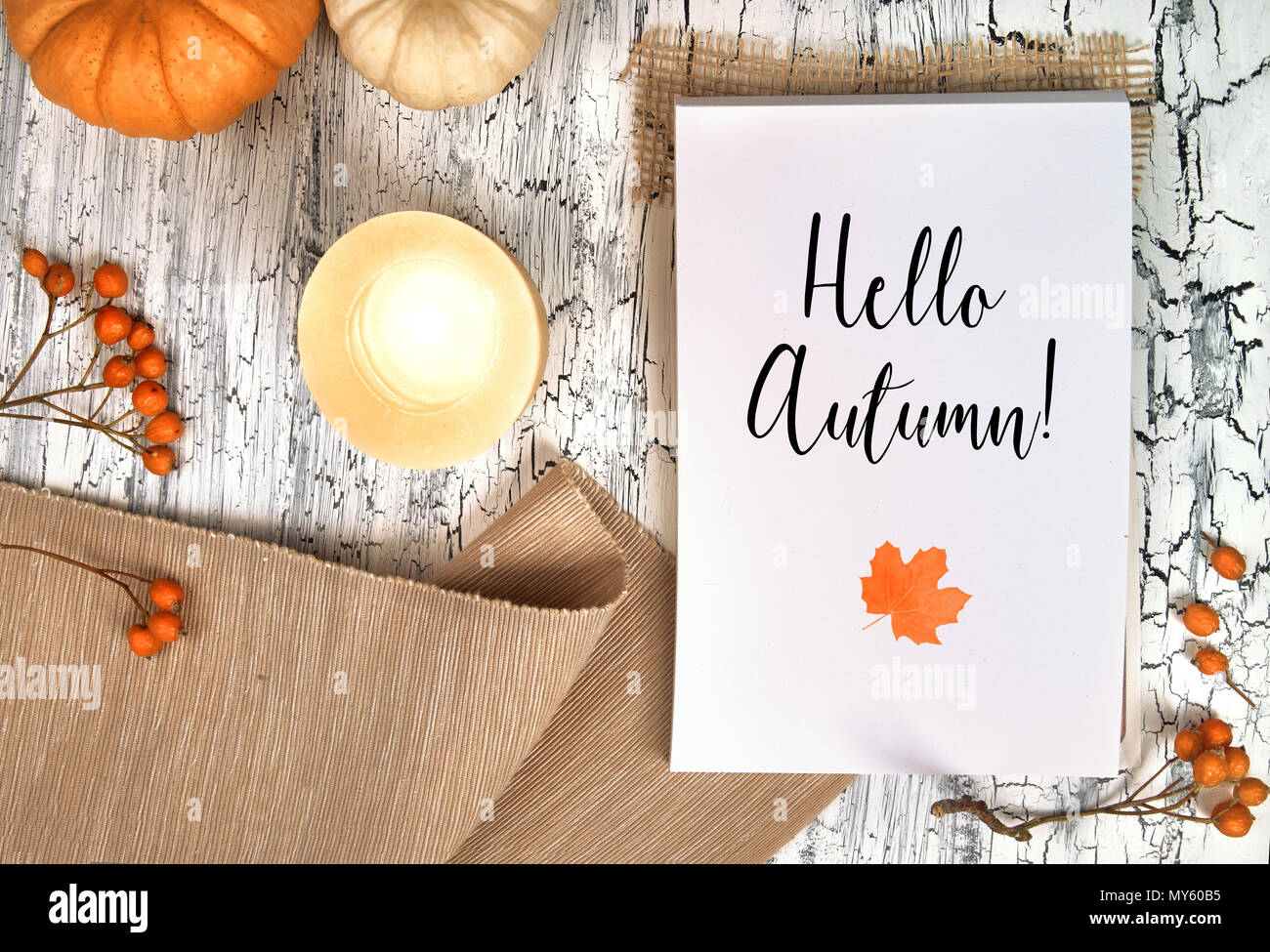 Bloc note blanc avec texte écrit 'Bonjour' et un marple laisser sur table rustique. Décorations d'automne autour de : la citrouille, la bougie allumée, serviette et être Banque D'Images