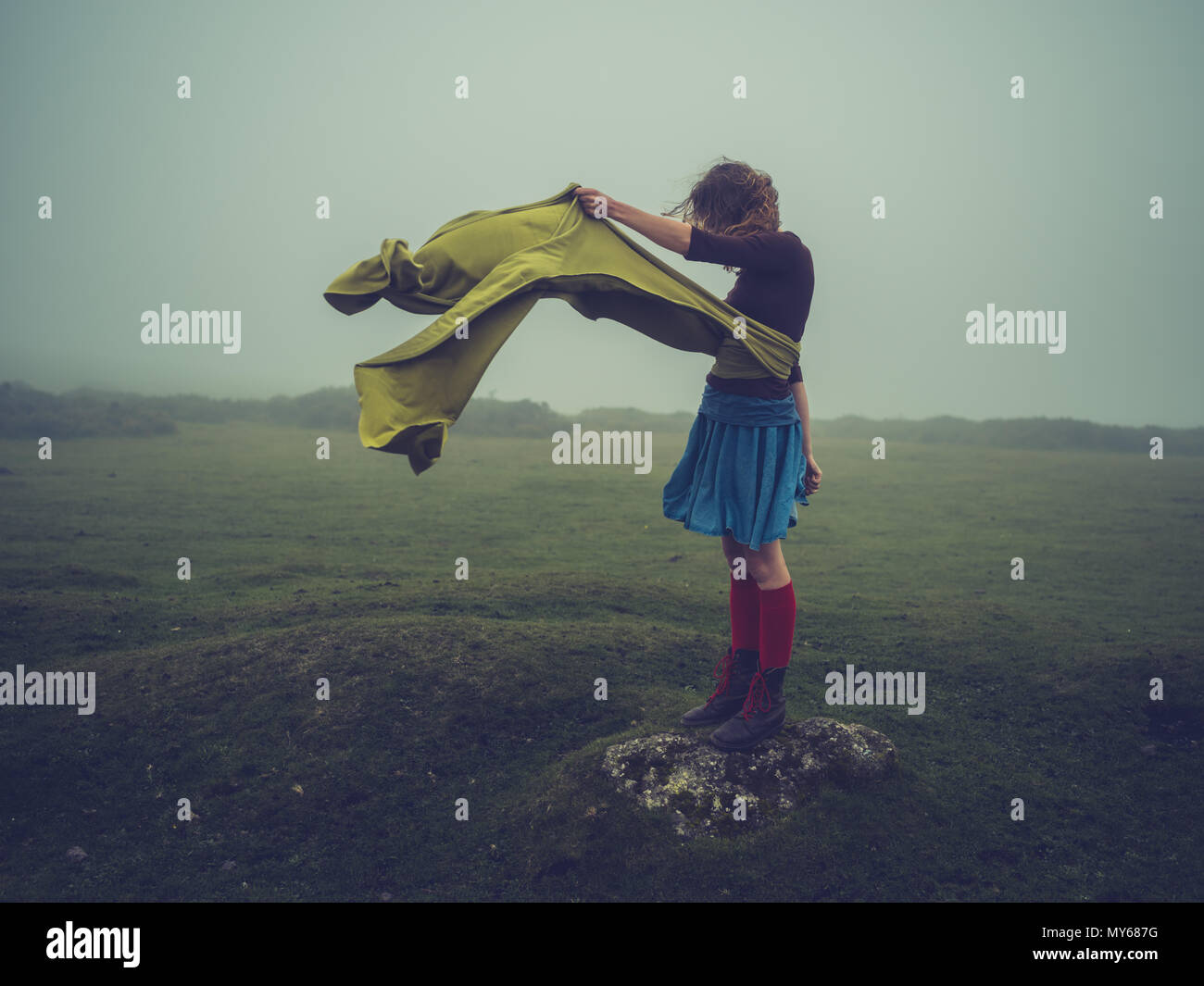 Une jeune femme avec une longue écharpe dans le vent est debout sur la lande dans le brouillard Banque D'Images