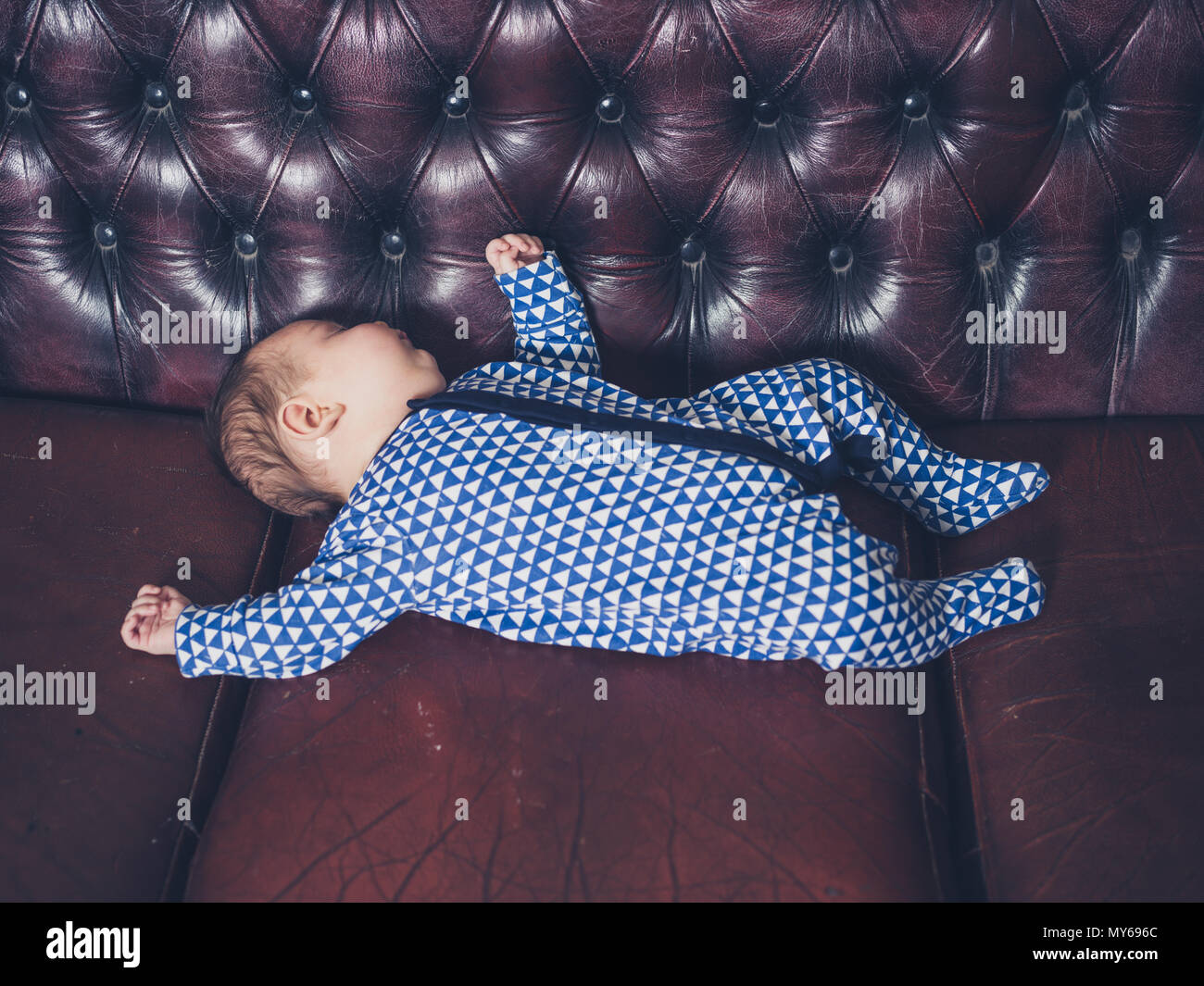 Un bébé dort par lui-même sur un canapé en cuir Banque D'Images