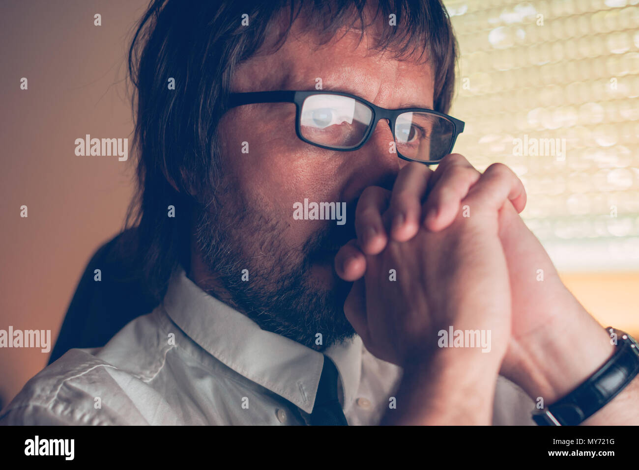 Face Close up portrait of businessman thinking concentré avec les mains jointes devant lui, dans l'intérieur bureau sombre. Inquiet et préoccupé bus mâle Banque D'Images