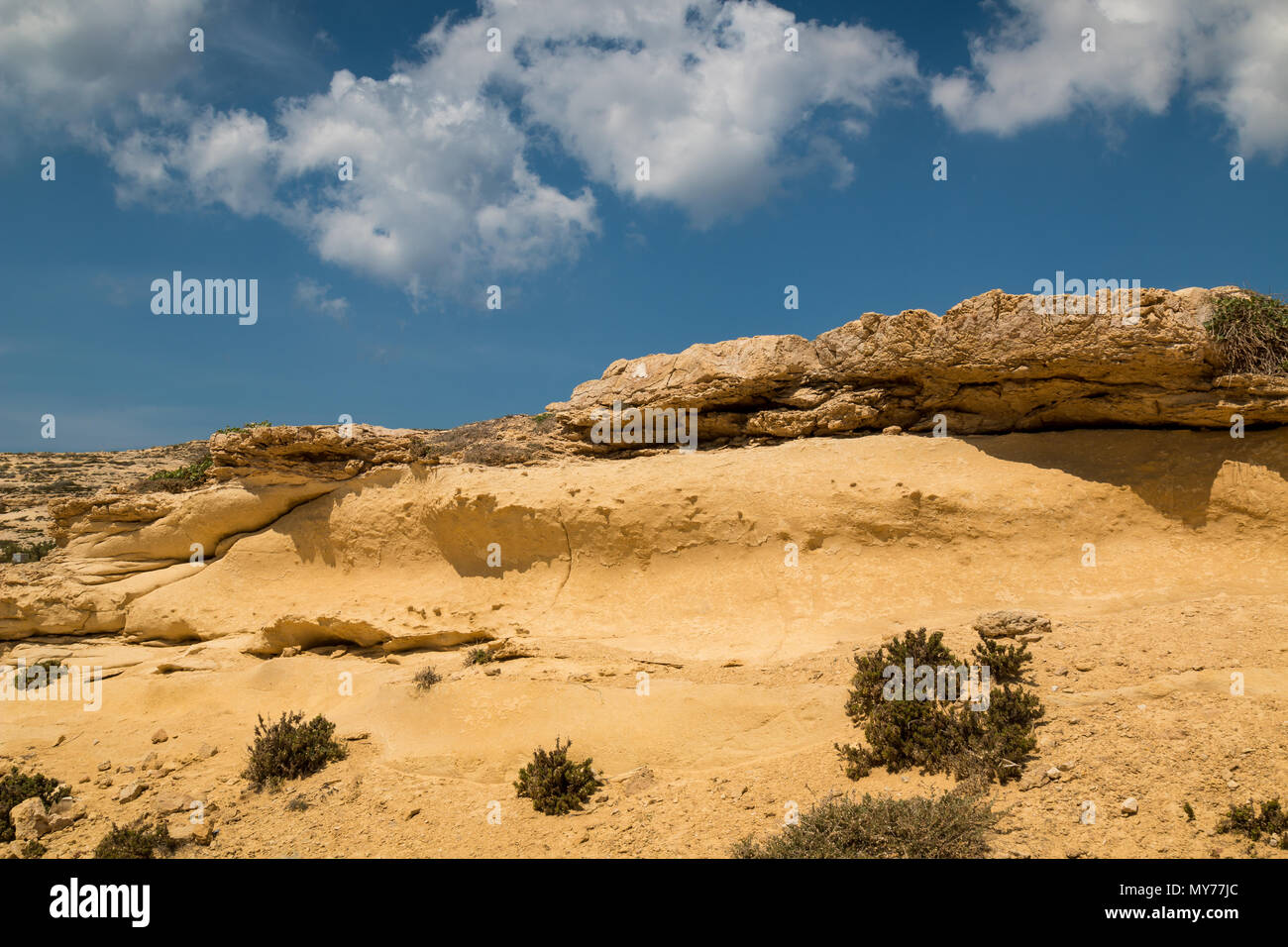 Montagnes Rocheuses sur la côte de l'île de Gozo, Malte. En partie recouverte d'un sable. Des touffes de végétation. Ciel bleu avec des nuages blancs. Banque D'Images