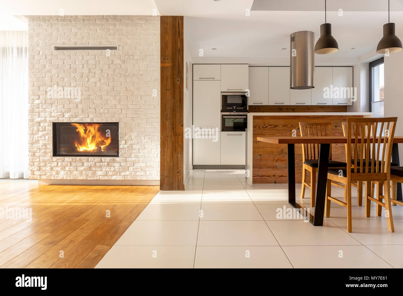 Cheminée dans les chambres spacieuses de l'intérieur de la maison blanche avec des chaises en bois à la table près de la cuisine. Photo réelle Banque D'Images