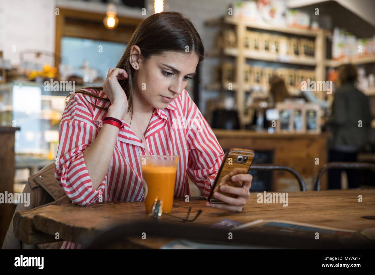 Jeune femme assise dans un café, l'utilisation de smartphone, le smoothie table devant elle Banque D'Images