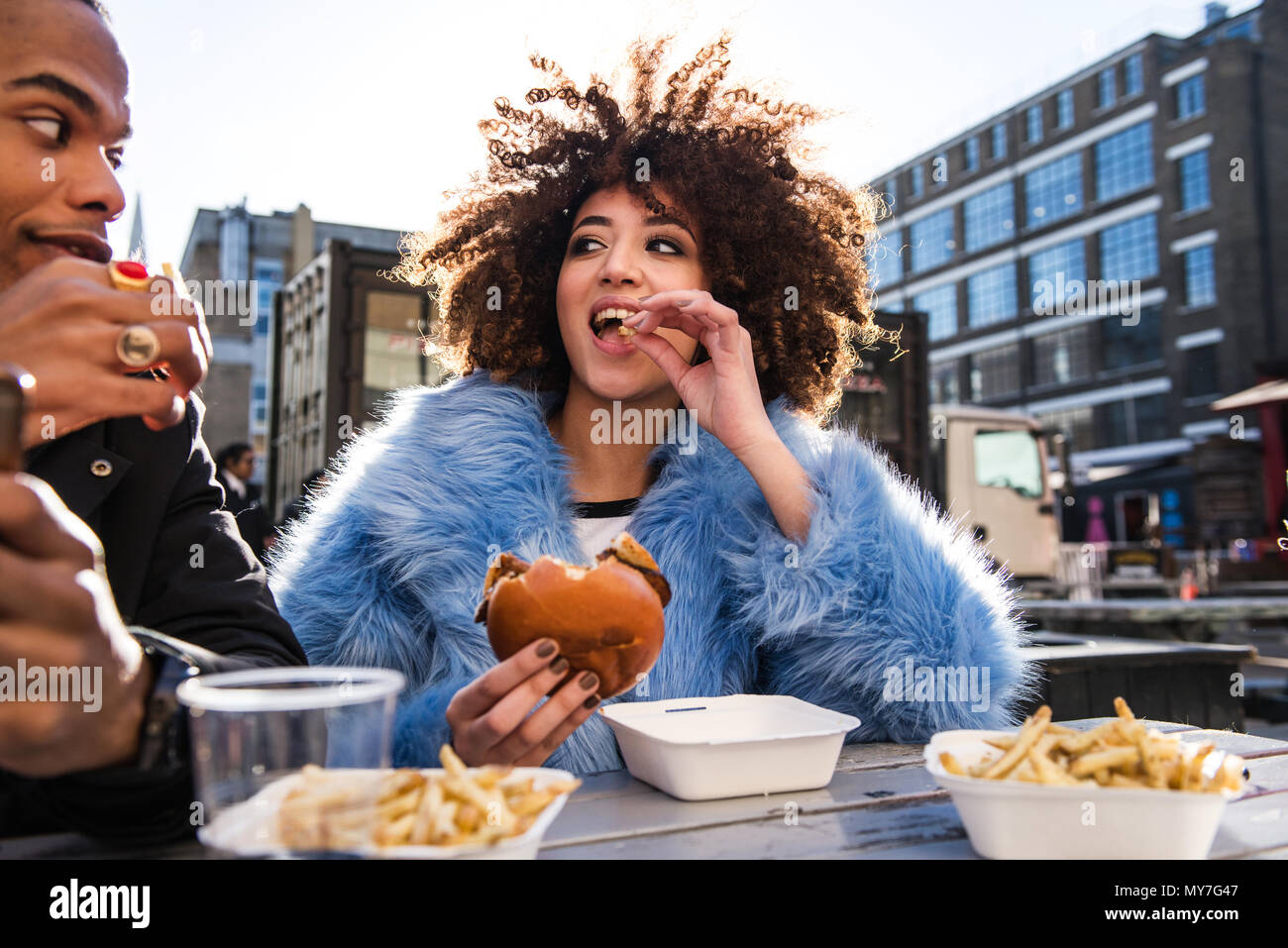 Jeune couple eating hamburger et frites à l'extérieur Banque D'Images