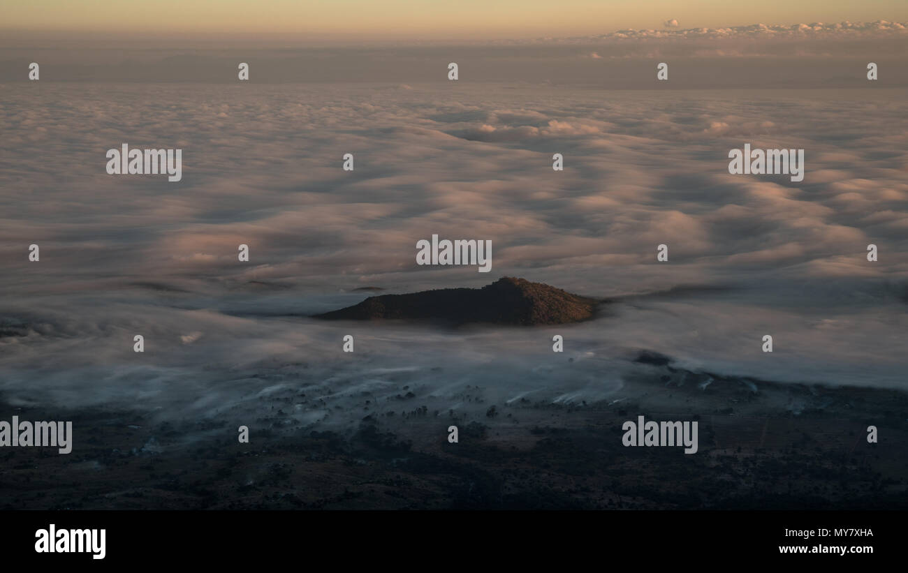 Une famille hill peeking through une mer de nuages à l'aube. Banque D'Images