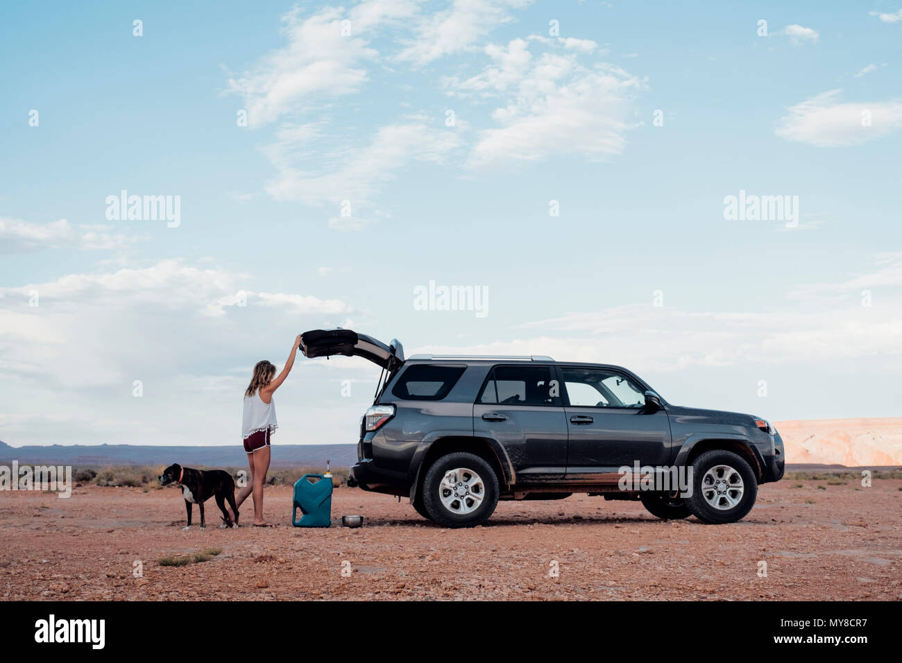 Jeune femme dans le réglage à distance, ouverture du coffre de SUV, à côté de son chien, Mexican Hat, Utah, USA Banque D'Images