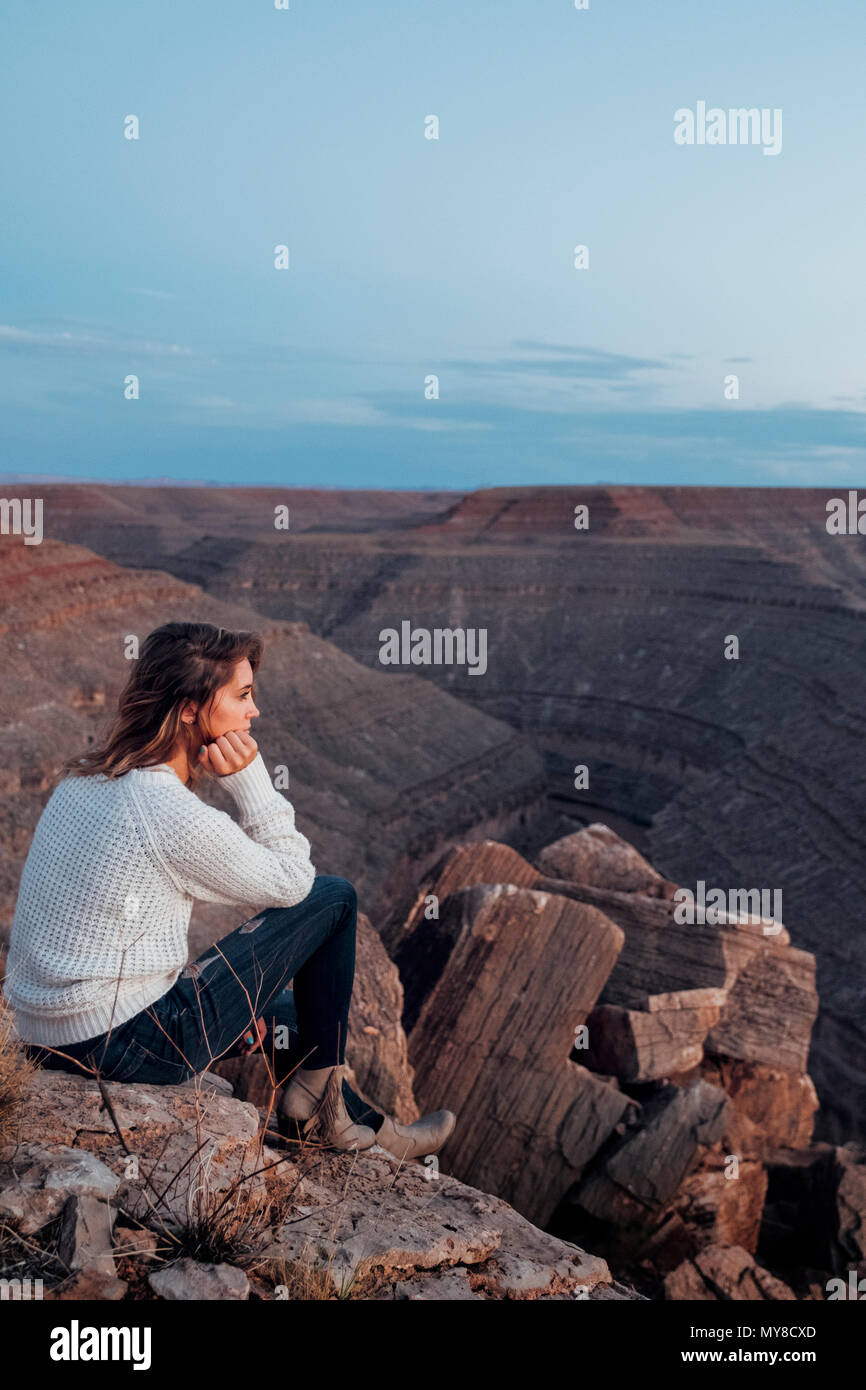 Jeune femme dans le réglage à distance, assis sur des rochers, à la vue, à Mexican Hat, Utah, USA Banque D'Images