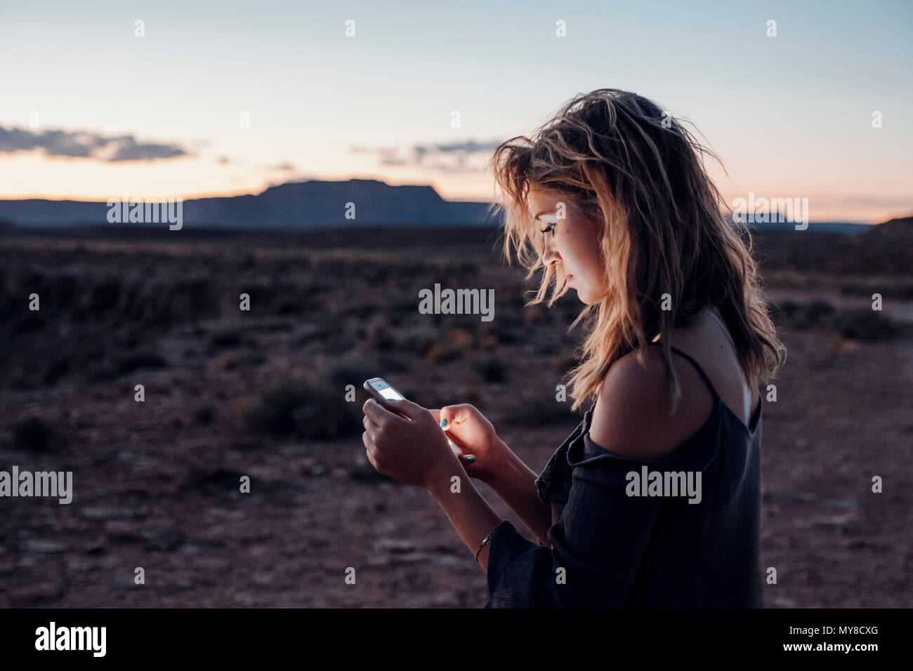 Jeune femme dans le réglage à distance, en utilisant smartphone, Mexican Hat, Utah, USA Banque D'Images