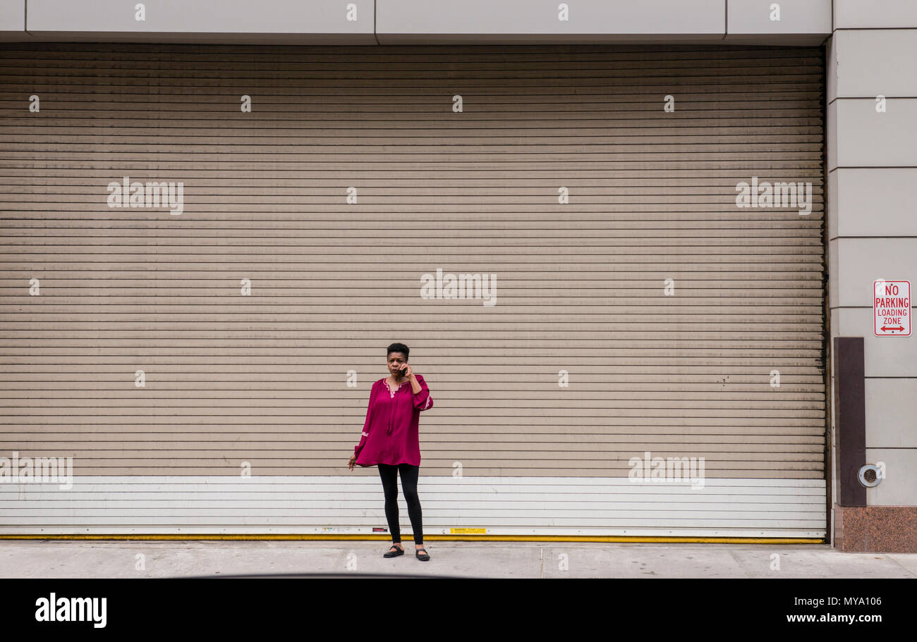 Utilisation du téléphone, femme debout devant des immenses, fermé, l'obturateur métallique, New York City, USA. Banque D'Images
