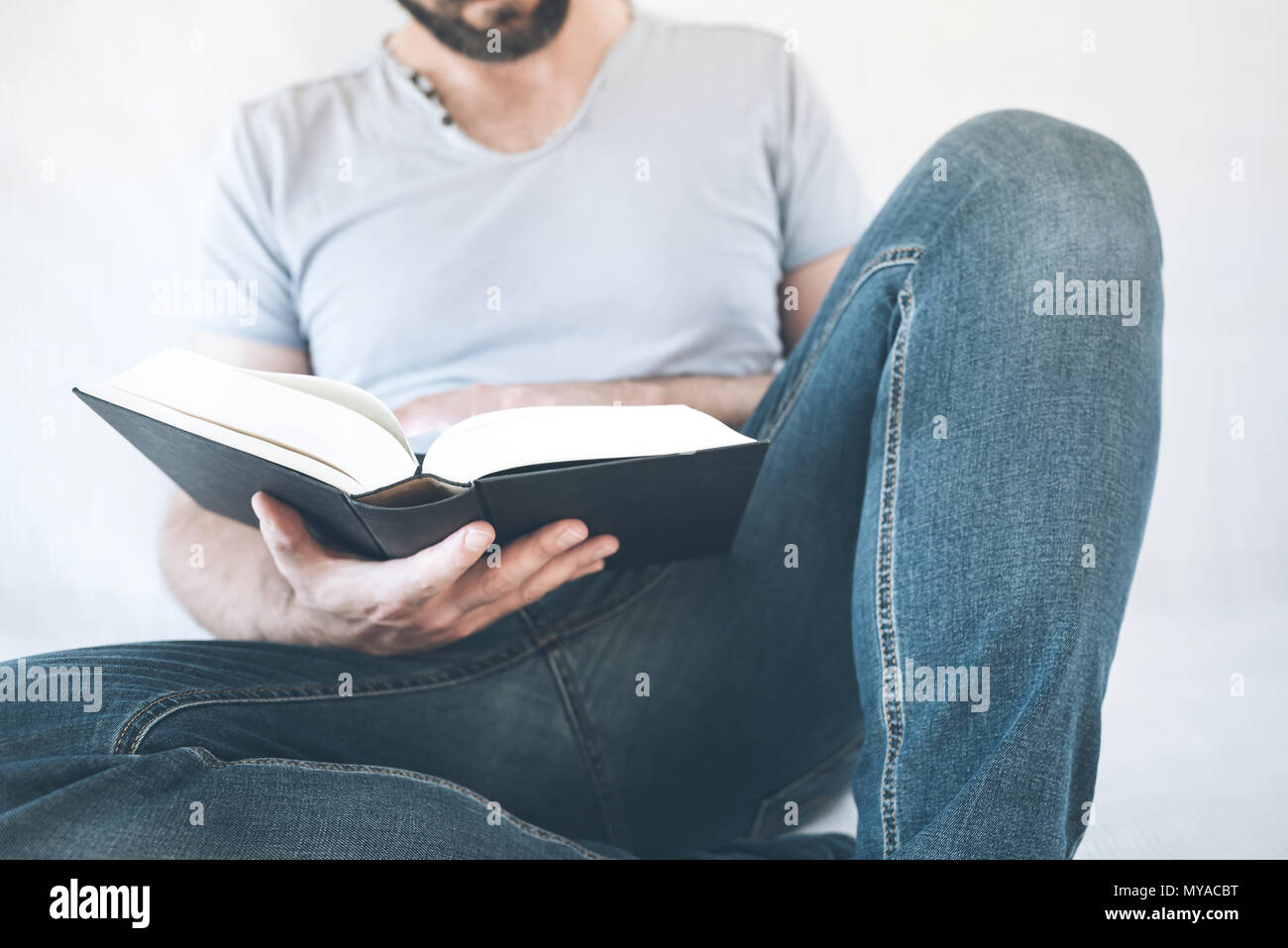Close-up of man relaxing on sofa reading a book Banque D'Images