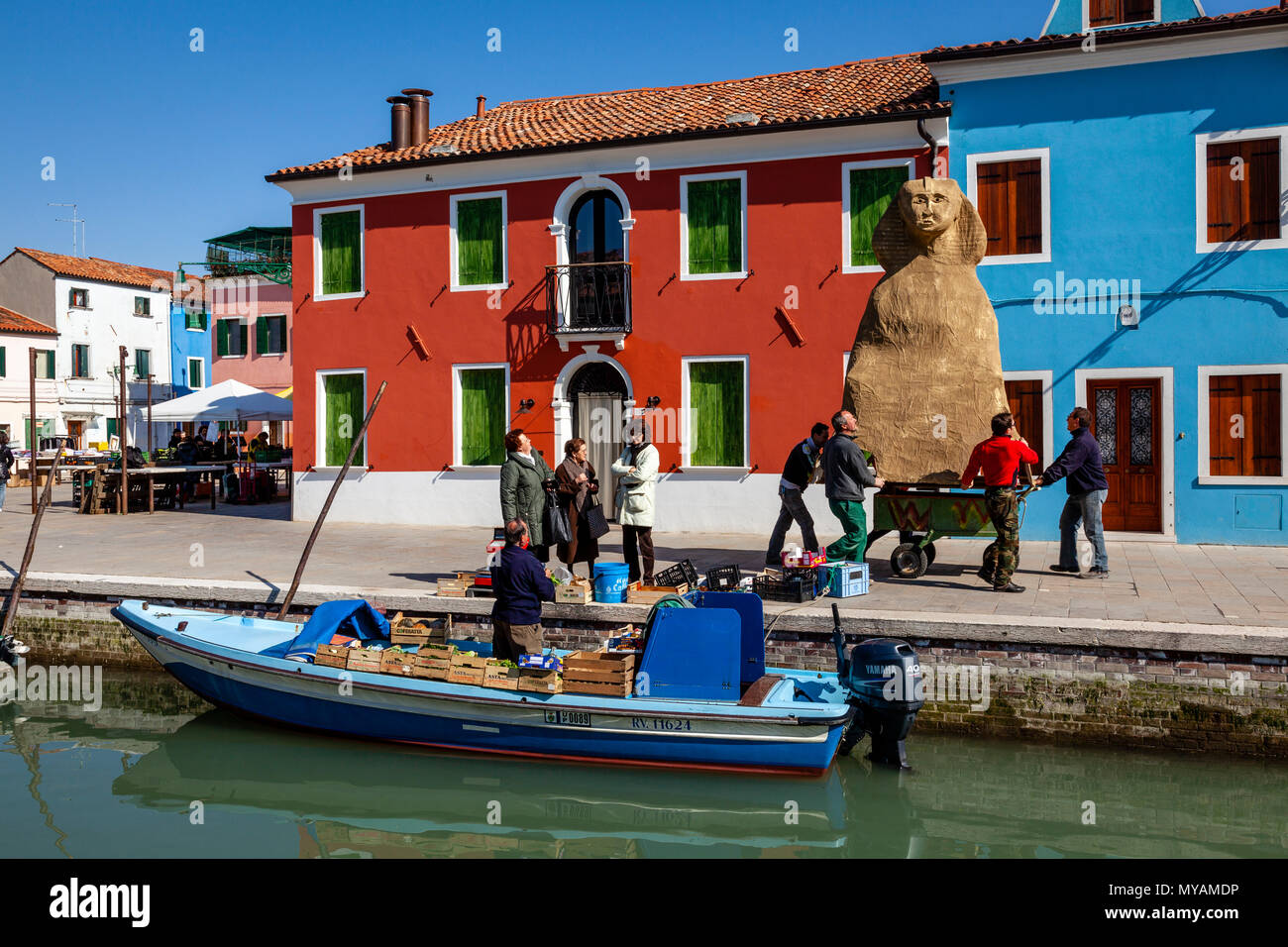 Les femmes achètent des fruits et légumes frais d'un magasin mobile comme un groupe d'hommes poussent un carnaval flotter le long de la rue, l'île de Burano, Venise, Italie Banque D'Images