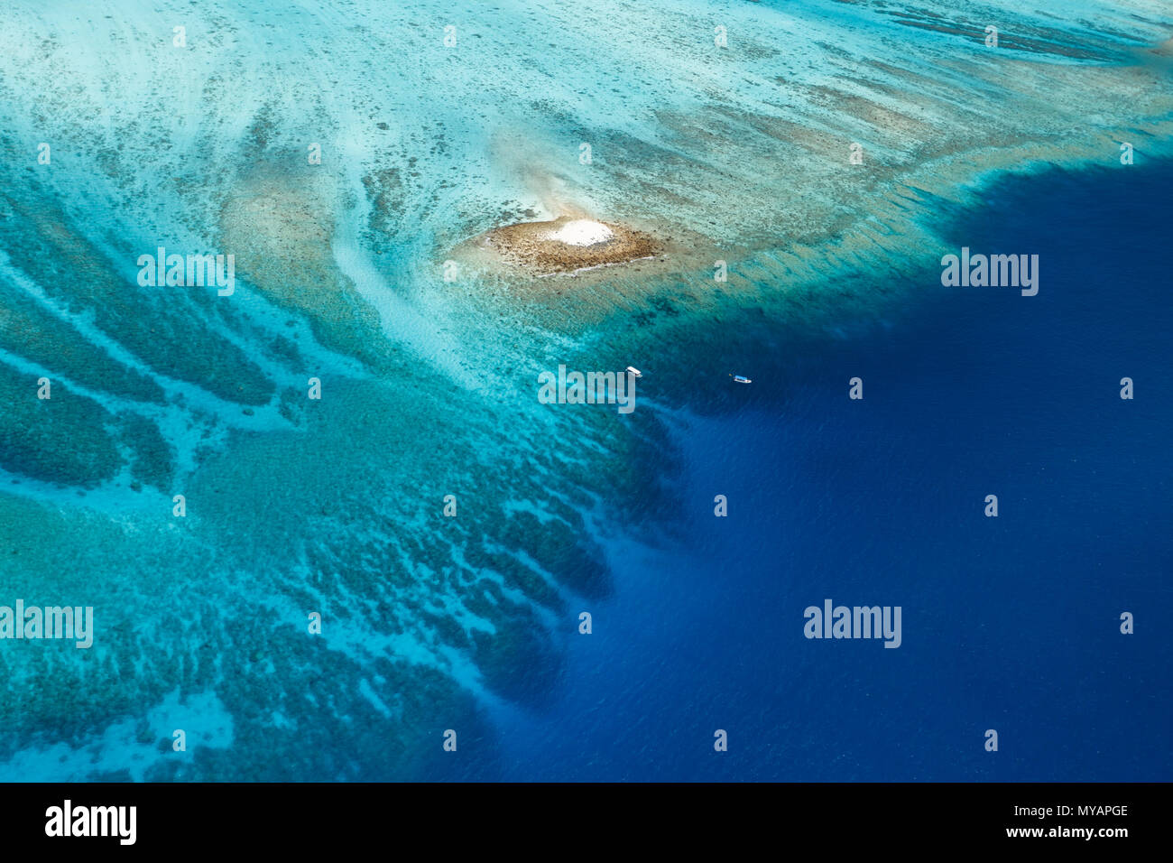 Vue aérienne d'un grand récif corallien coloré entourant une minuscule île de sable blanc avec deux bateaux à proximité Banque D'Images