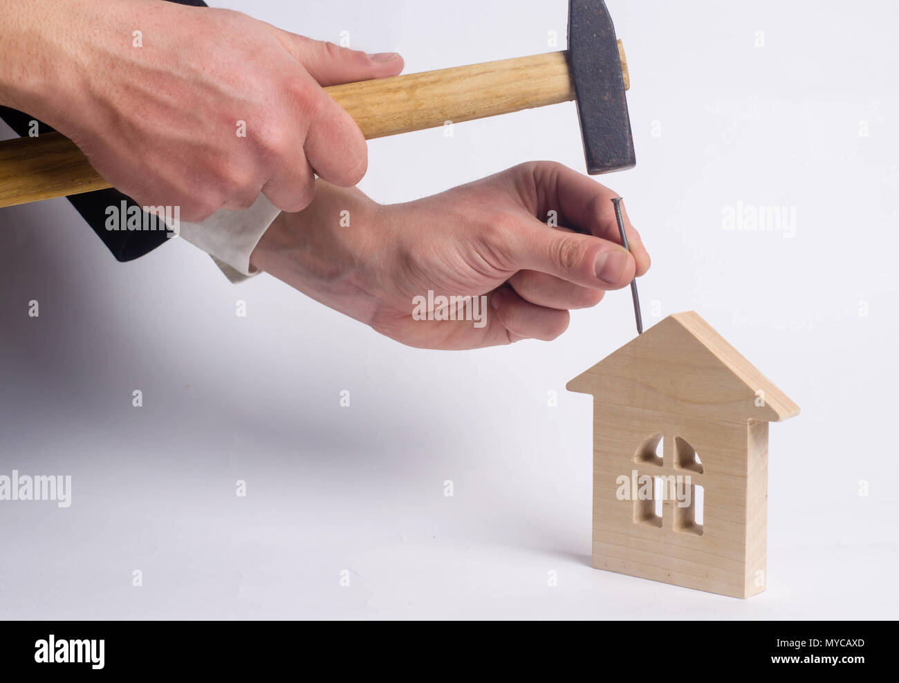 Marteaux homme un clou avec un marteau dans une maison en bois miniature sur un fond blanc. Concept de la réparation des maisons. Le travailleur effectue des travaux de réparation dans th Banque D'Images
