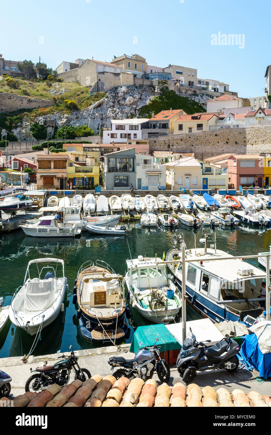 Le petit port du Vallon des Auffes à Marseille par un matin ensoleillé avec des bateaux amarrés devant cabanons colorés et maisons en dessous de la falaise. Banque D'Images