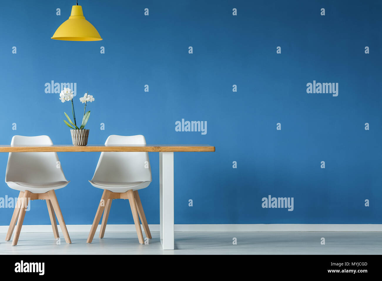 Deux chaises, fleur, jaune et bleu sur une table en bois, mur vide à l'intérieur de salle à manger Banque D'Images