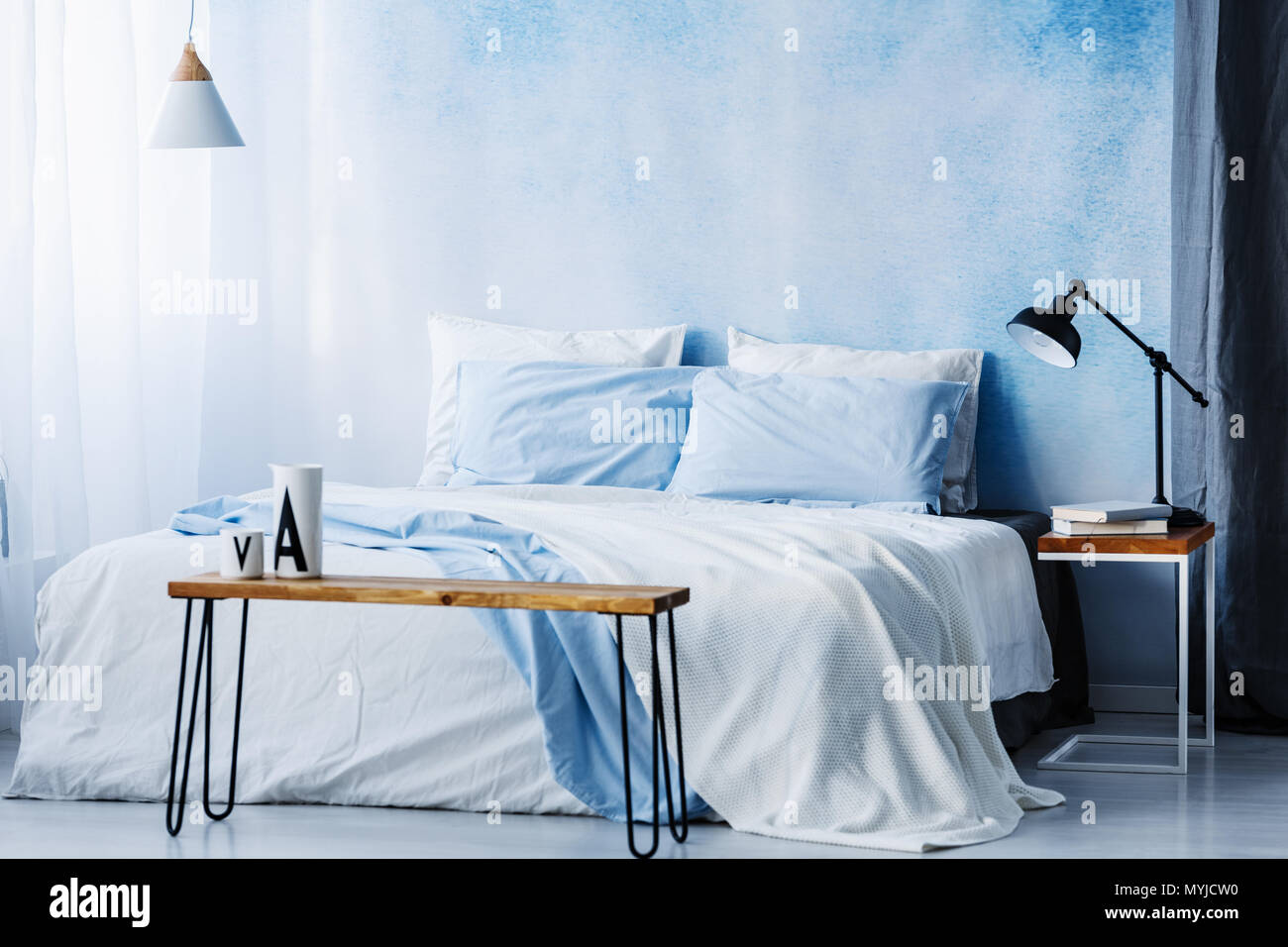 Lampe au-dessus de table en bois en face de lit avec couverture bleue  pastel à l'intérieur chambre à coucher Photo Stock - Alamy