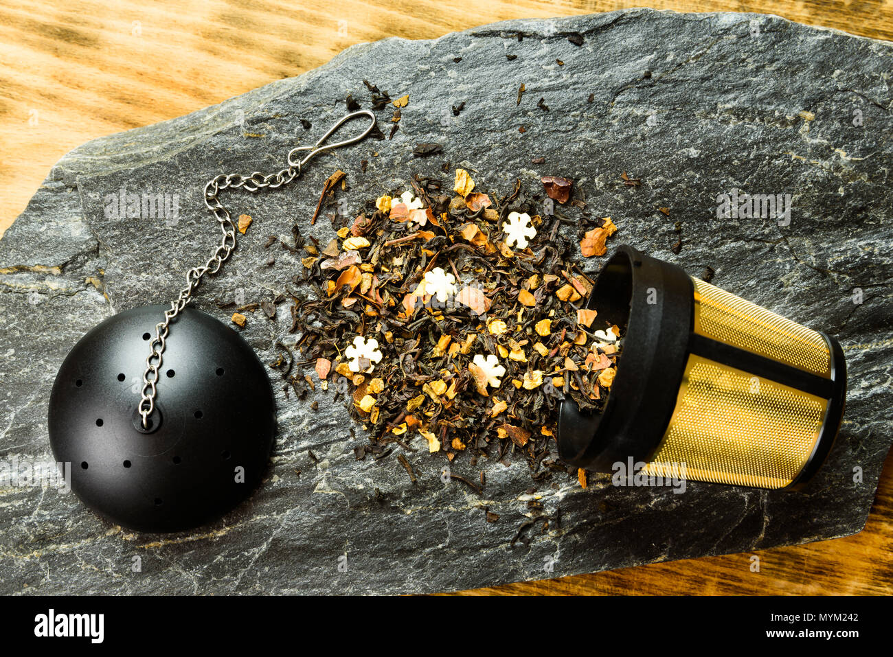 Thé noir aromatisé dispersés à l'extérieur d'un infuseur à thé plaqué or sur une dalle de pierre. Couvercle avec la chaîne à l'autre. Banque D'Images