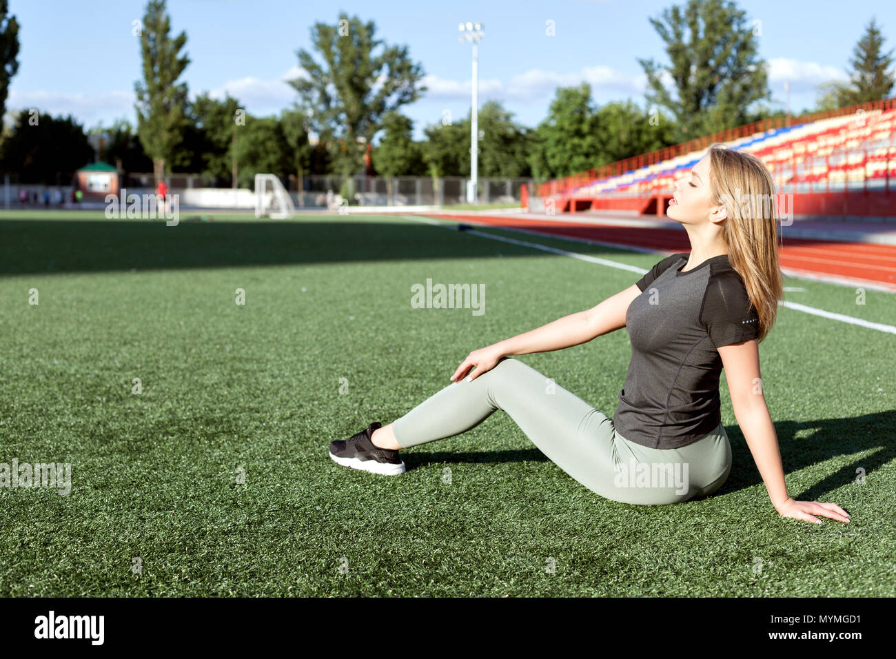 Jeune femme dans les vêtements de sport assis sur l'herbe dans le stade. Banque D'Images