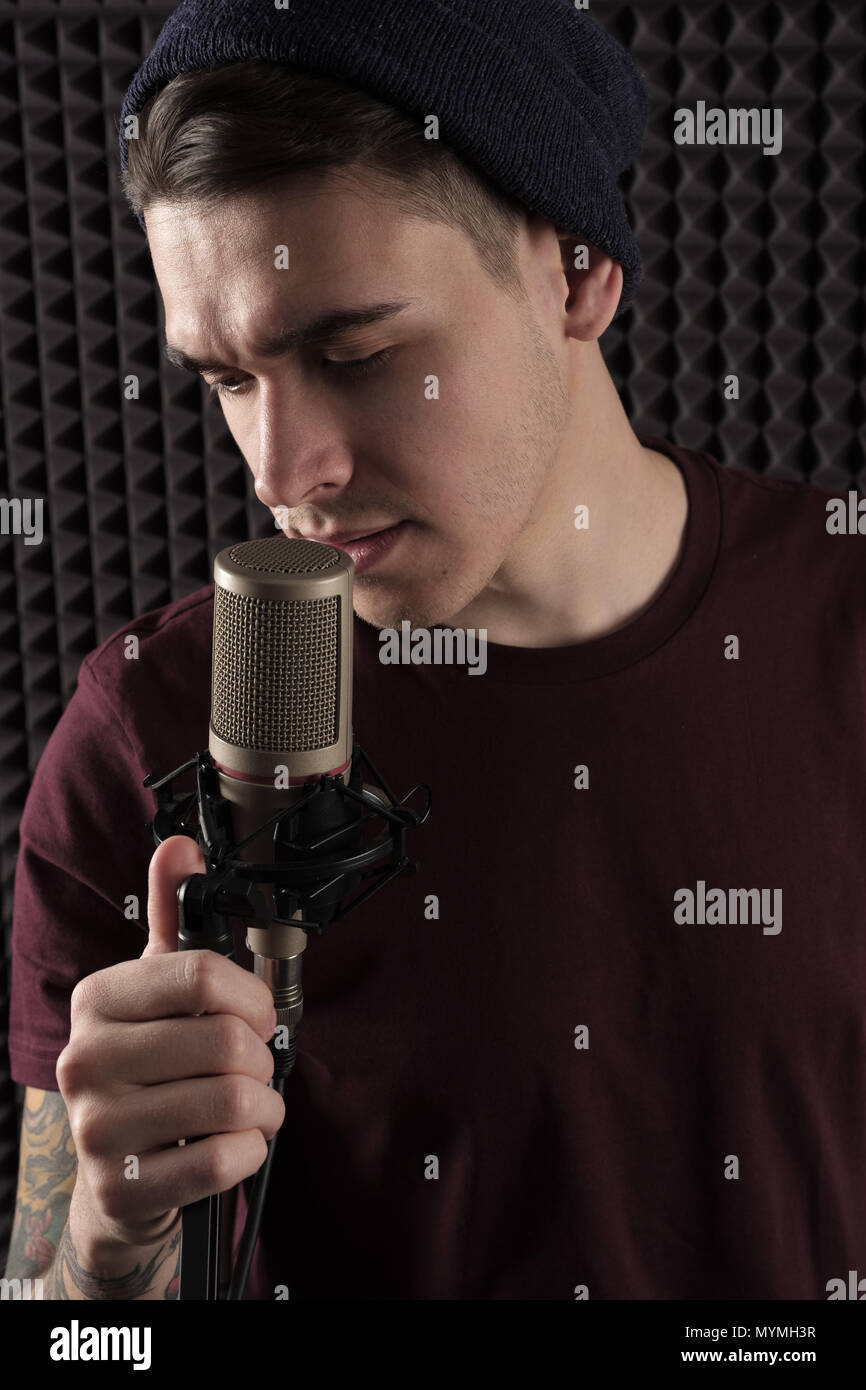 Un portrait d'un mec qui chante au guichet avec un microphone et le maintient d'une main. Photo verticale Banque D'Images