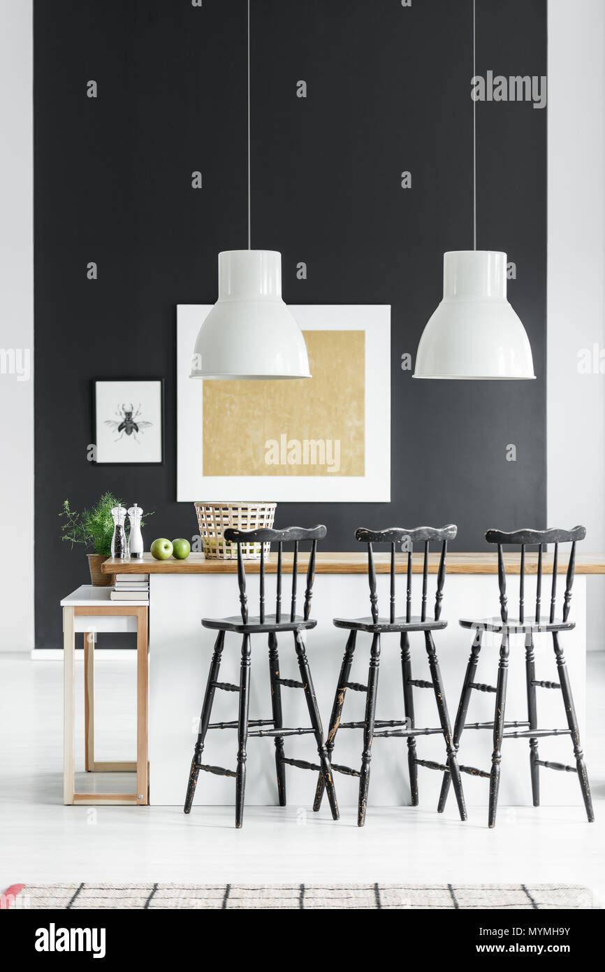 Lampes blanches au-dessus de comptoir avec tabourets de bar noir en cuisine avec peinture l'or sur le mur noir Banque D'Images
