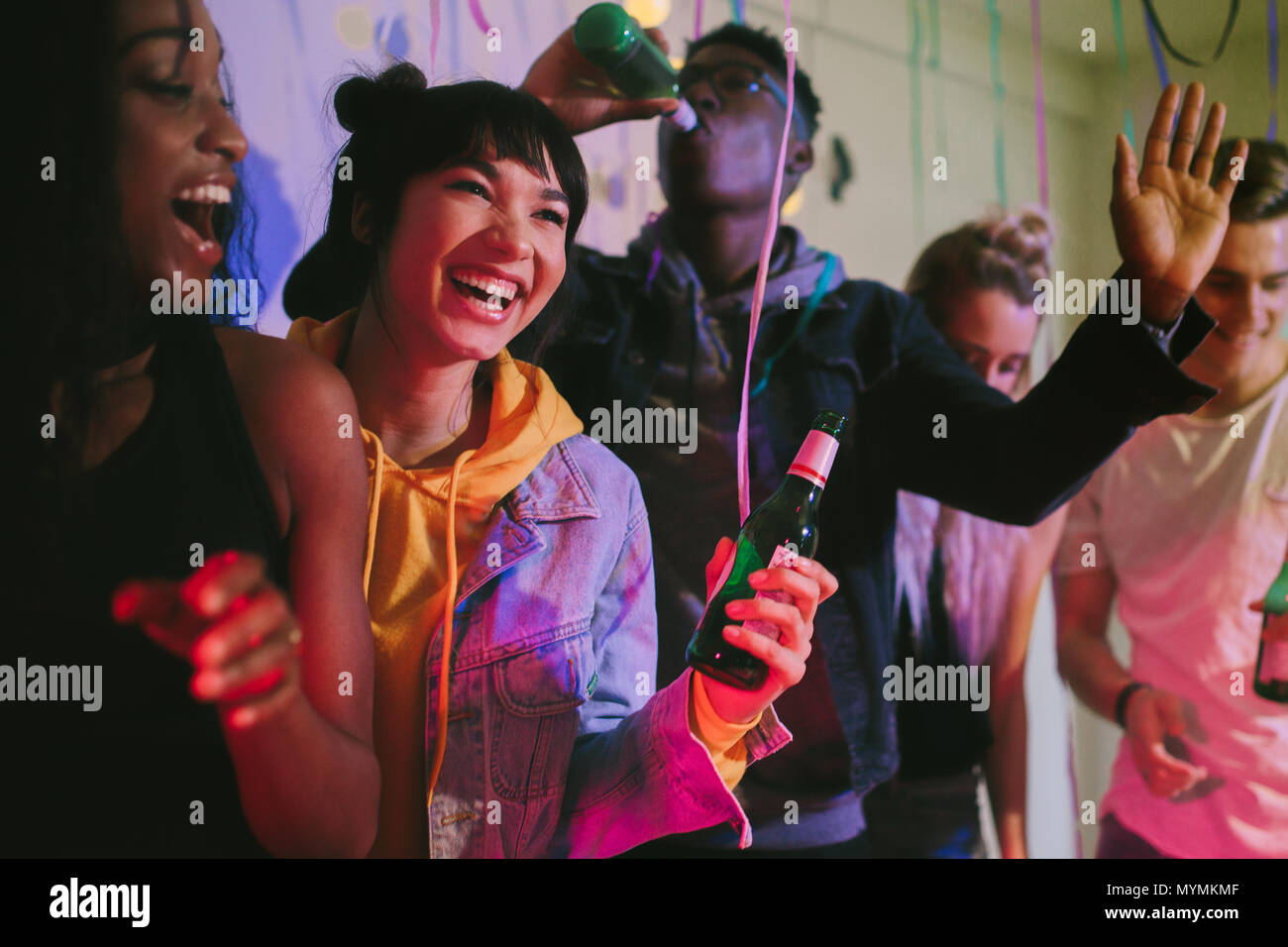 Les jeunes hommes et femmes bénéficiant à la house party. Les amis de rire et danser holding drinks à la partie. Banque D'Images