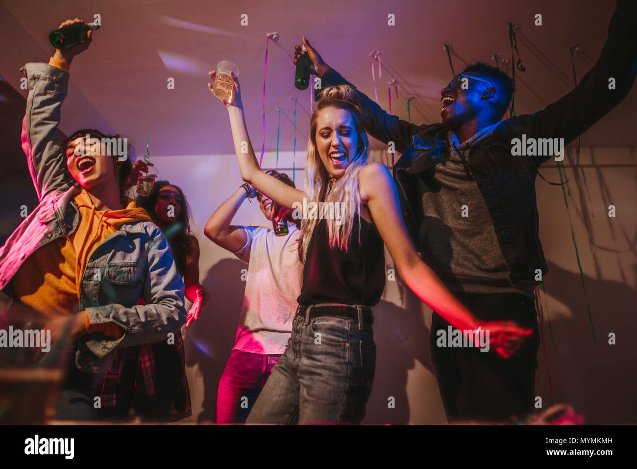 Les jeunes hommes et femmes s'amusant lors d'une maison colorée partie. Les amis de la danse dans la joie holding drinks à une house party. Banque D'Images