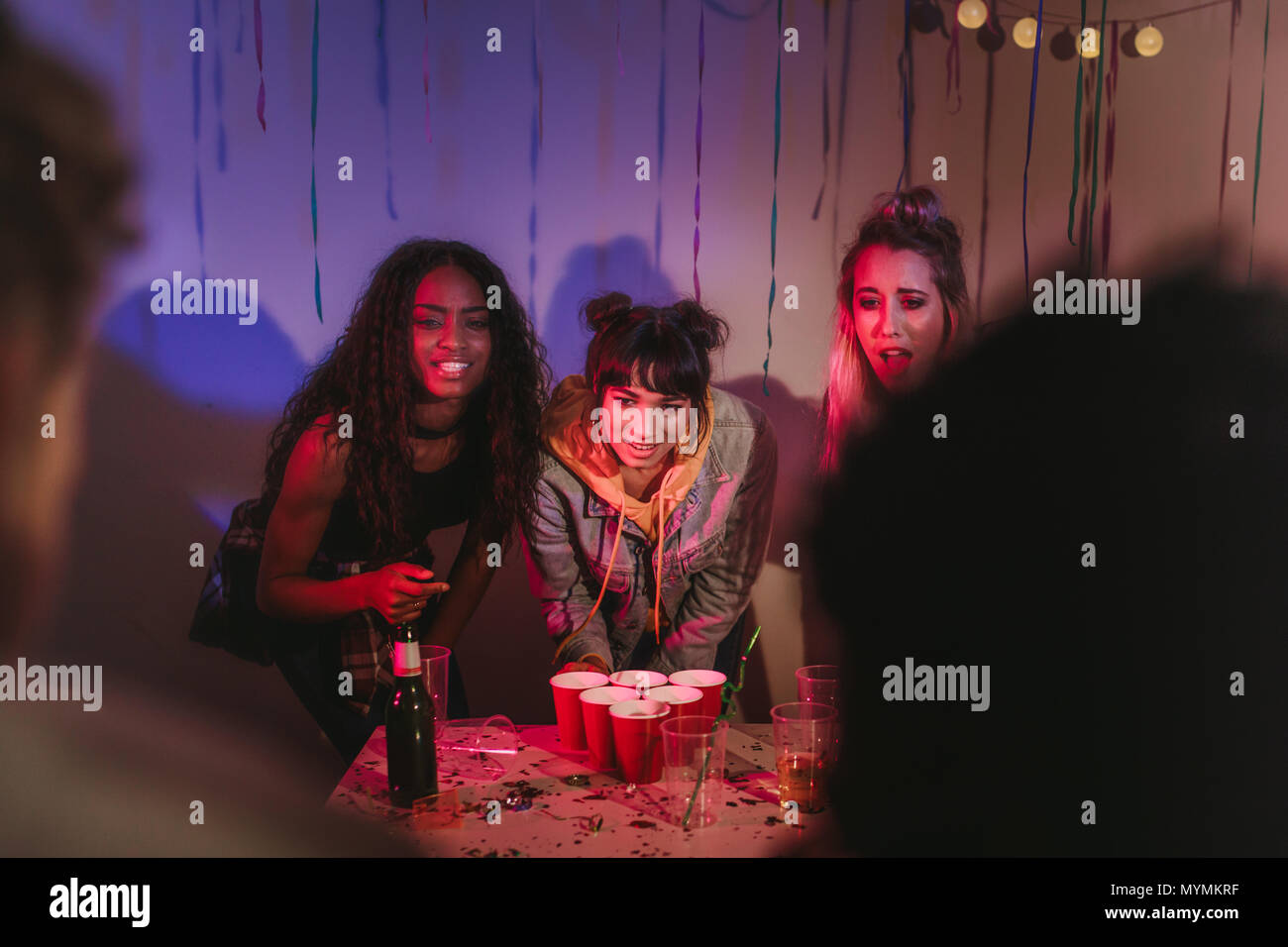 Trois jeunes femmes debout à une table avec des verres et une bouteille a organisé la fête. Les amis s'amusant à une chambre colorée avec partie decora Banque D'Images