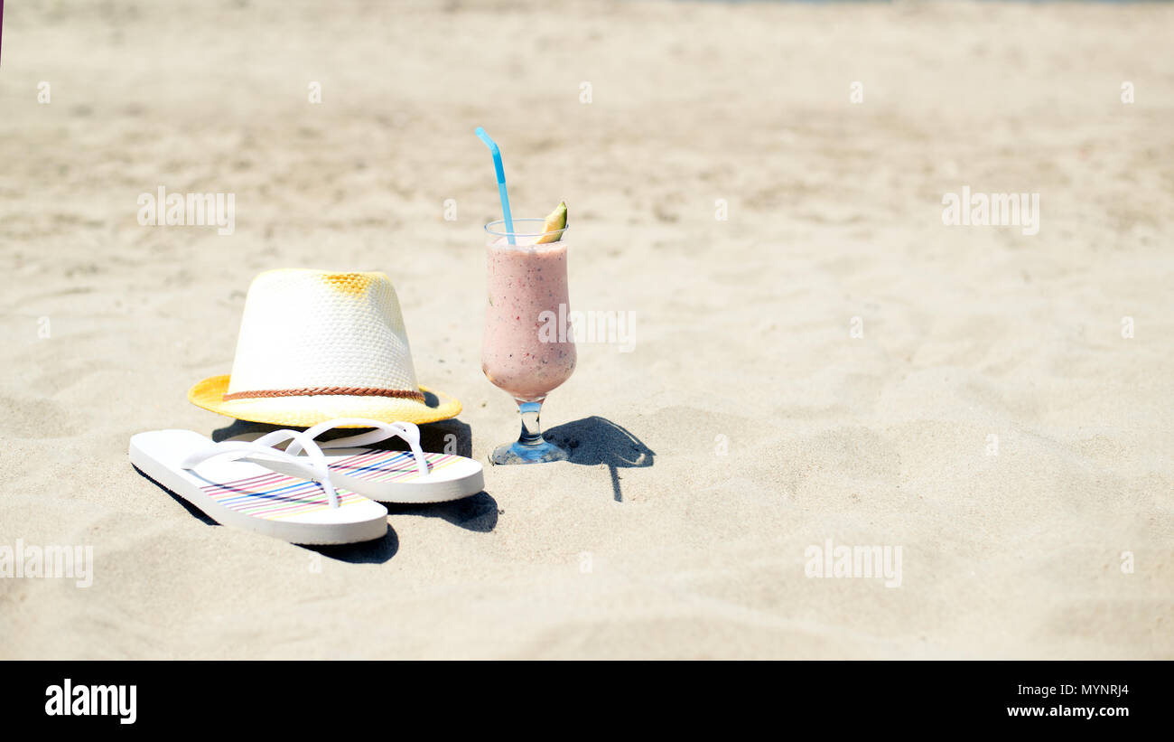 Smoothie fraise jus frais, un chapeau et des chaussons près de la mer sur une plage de sable Banque D'Images
