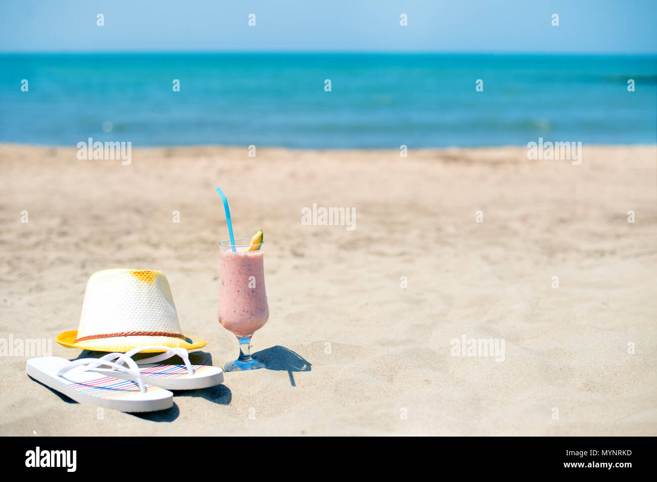 Smoothie fraise jus frais, un chapeau et des chaussons près de la mer sur une plage de sable Banque D'Images