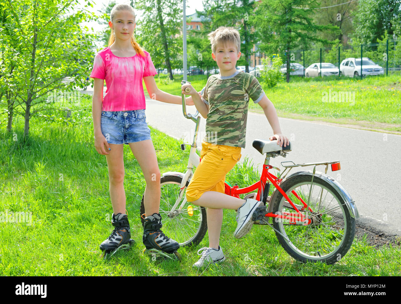 Après-midi d'été chaud. Vacances actives en famille d'adolescents-frère et soeur avec patins à roulettes et un vélo Banque D'Images