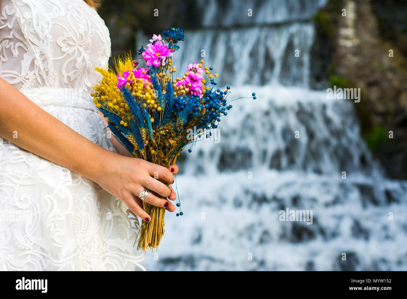 Bride holding bouquet de mariage coloré en face d'une cascade Banque D'Images