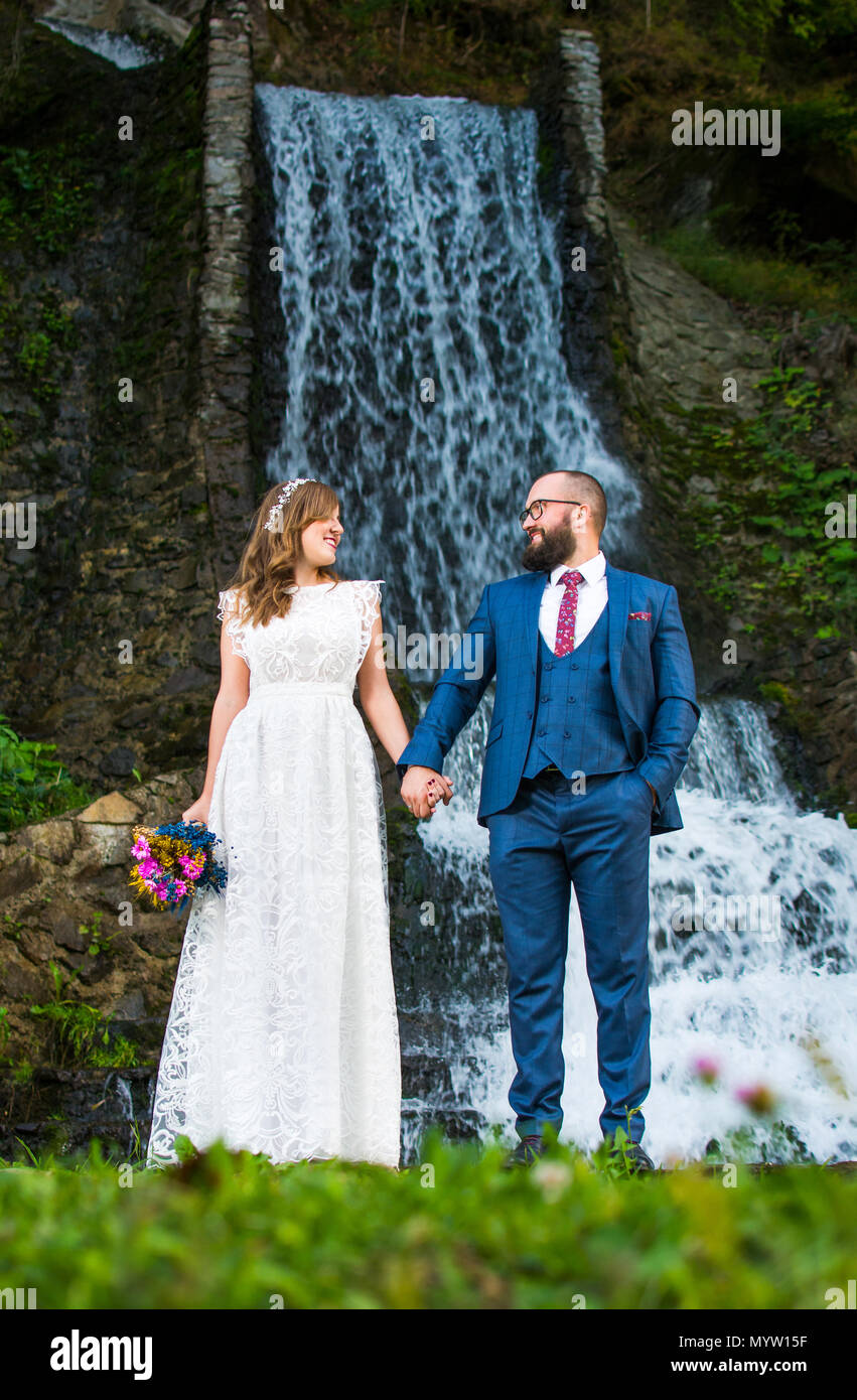 Bride and Groom holding hands en face d'une cascade Banque D'Images