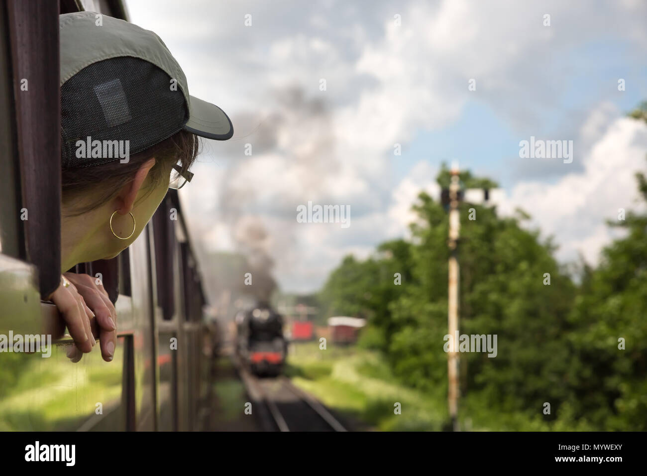 Vue arrière, une femme passager s'est penchée devant la fenêtre en voyageant sur le train à vapeur Severn Valley Railway, ancien Royaume-Uni, à l'approche de la gare vintage en été. Banque D'Images