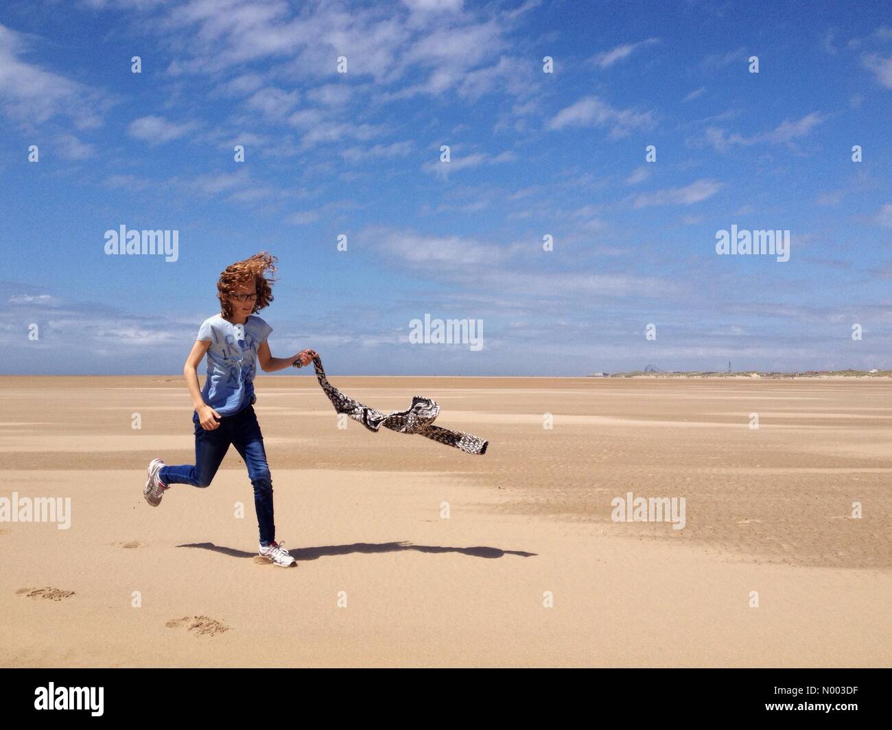 28 juin temps ensoleillé mais venteux sur la plage à Lytham St Anne's dans le Lancashire. Jeune fille courir le long beach transportant son manteau dans le vent. Banque D'Images 28 juin temps ensoleillé mais venteux sur la plage à Lytham St Anne's dans le Lancashire. Jeune fille courir le long beach transportant son manteau dans le vent. Banque D'Images