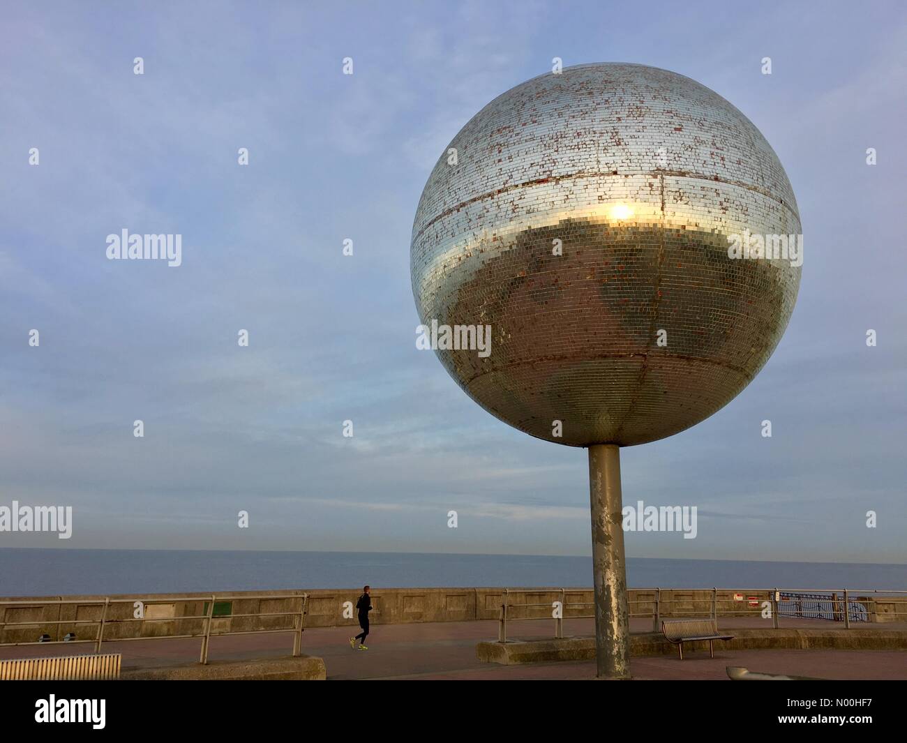 Météo Royaume-Uni : soleil brumeux à Blackpool. Ciel bleu et matinée froide sur Blackpool South Promenade alors que le jogger tôt le matin passe devant la sculpture géante de boule à paillettes. Banque D'Images Météo Royaume-Uni : soleil brumeux à Blackpool. Ciel bleu et matinée froide sur Blackpool South Promenade alors que le jogger tôt le matin passe devant la sculpture géante de boule à paillettes. Banque D'Images