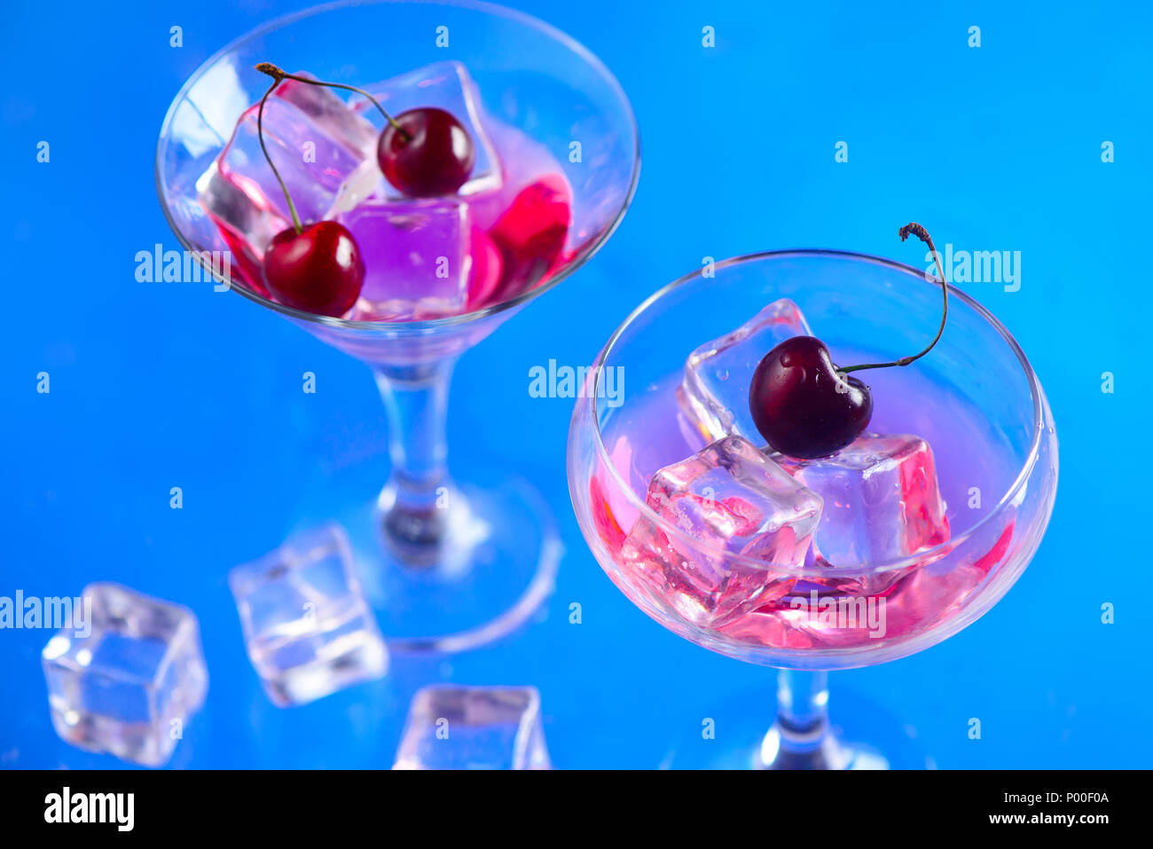 Verre verres à cocktail à la cerise avec des cubes de glace sur un fond bleu. Boisson fraîche avec copie espace. Concept de boissons d'été Banque D'Images