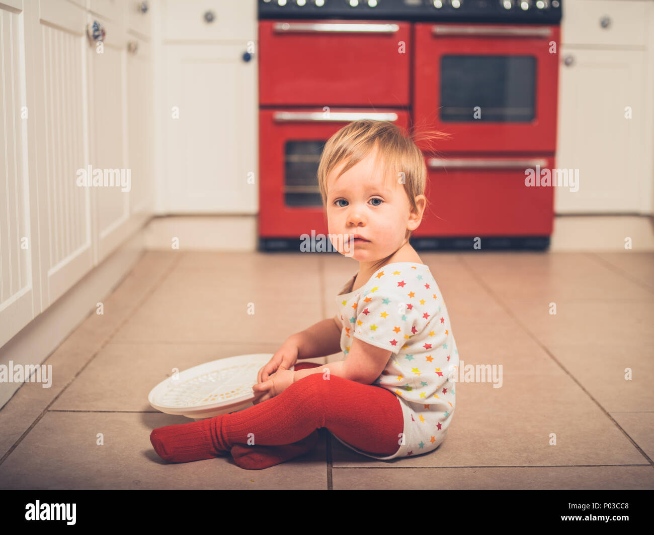 Un petit garçon est assis sur le plancher avec une essoreuse à salade Banque D'Images