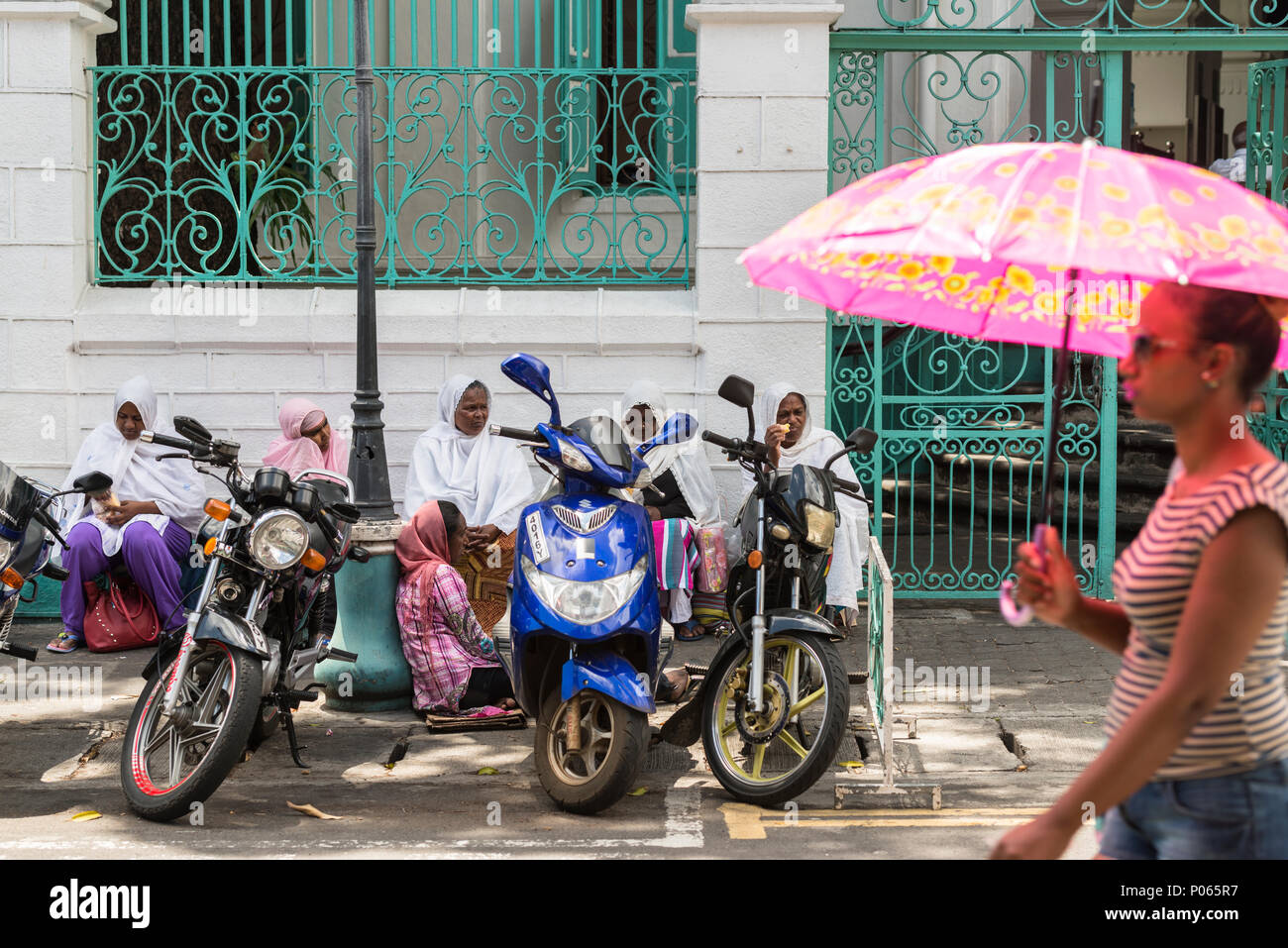 Une jeune femme en passant devant un groupe de femmes assis sur la rue en attente de l'aumône en dehors de Jummah Mosque un vendredi, Port Louis, Ile Maurice Banque D'Images