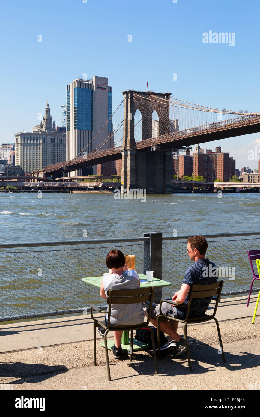 Couple sitting in Brooklyn Bridge park prendre un verre et à l'ensemble de l'East River à Manhattan dans le soleil du printemps New York USA Banque D'Images